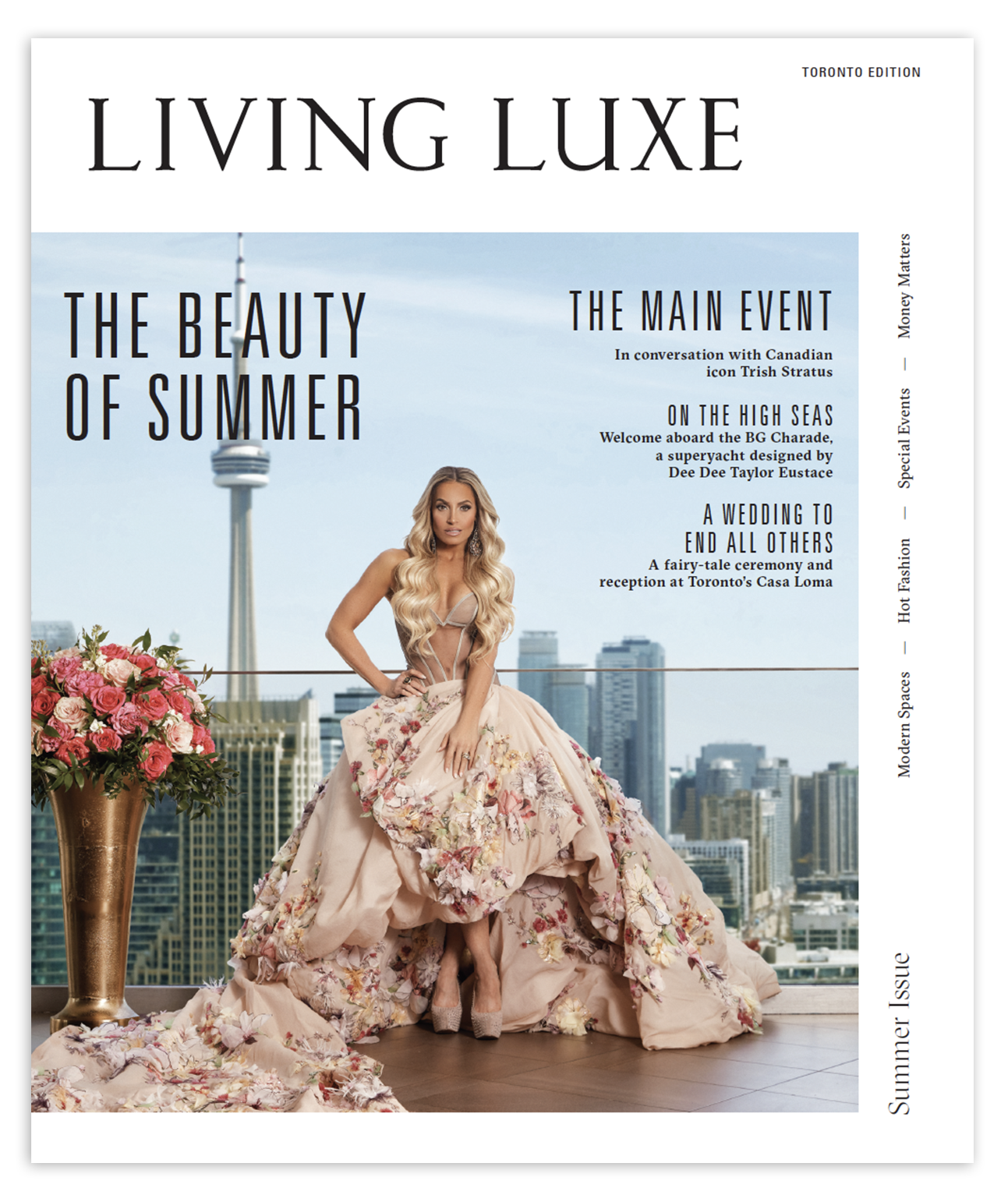 A woman in a floral ball gown standing on a balcony with a city skyline and CN Tower in the background with a large bouquet of pink roses to her left.