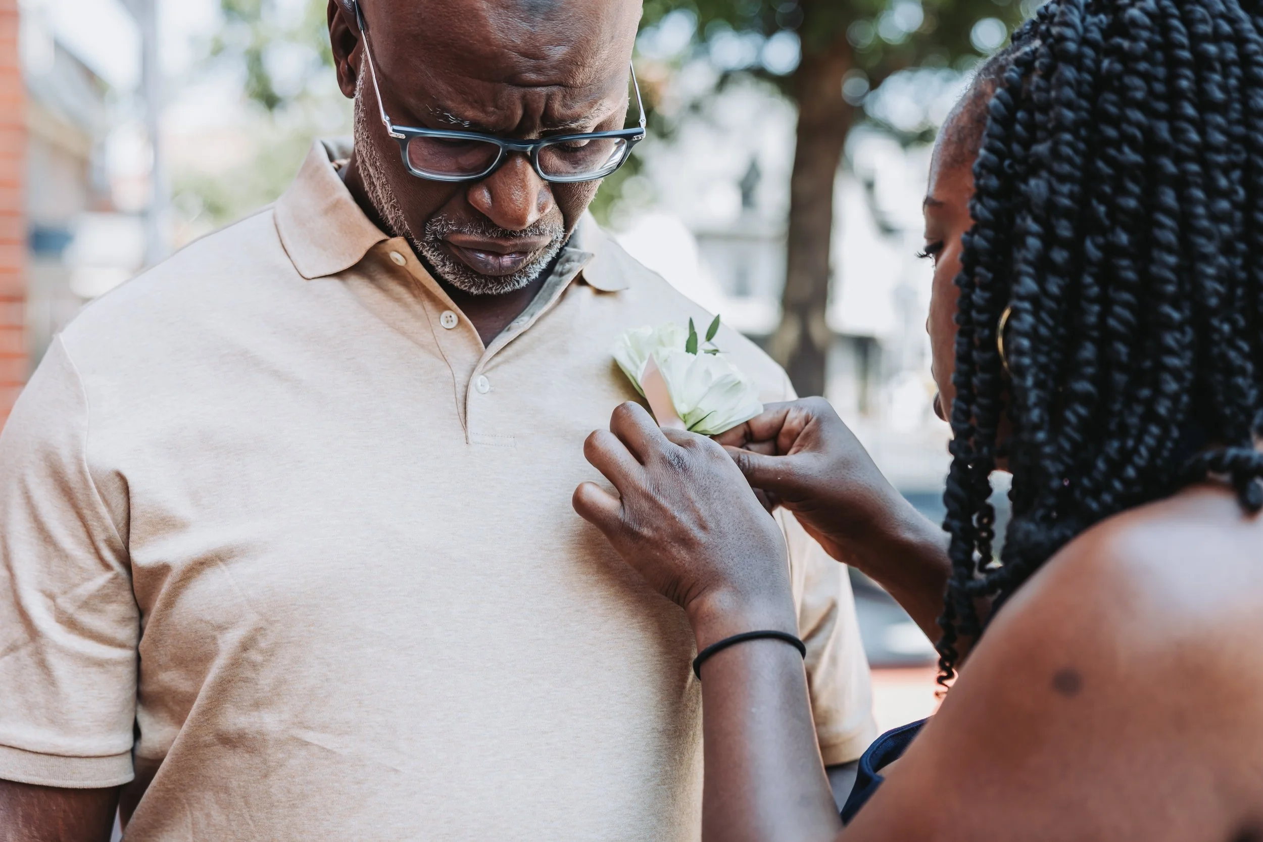 A woman is pinning a white flower onto a man's beige polo shirt during an outdoor event.