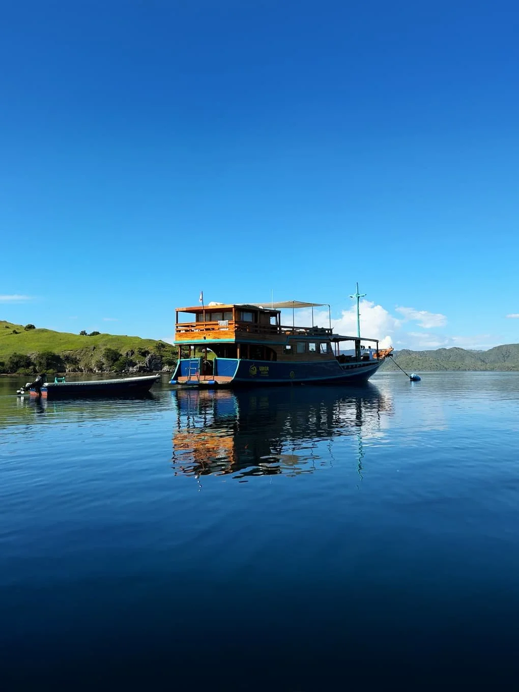 A boat floating on calm water, green hills in the background, and a clear blue sky.