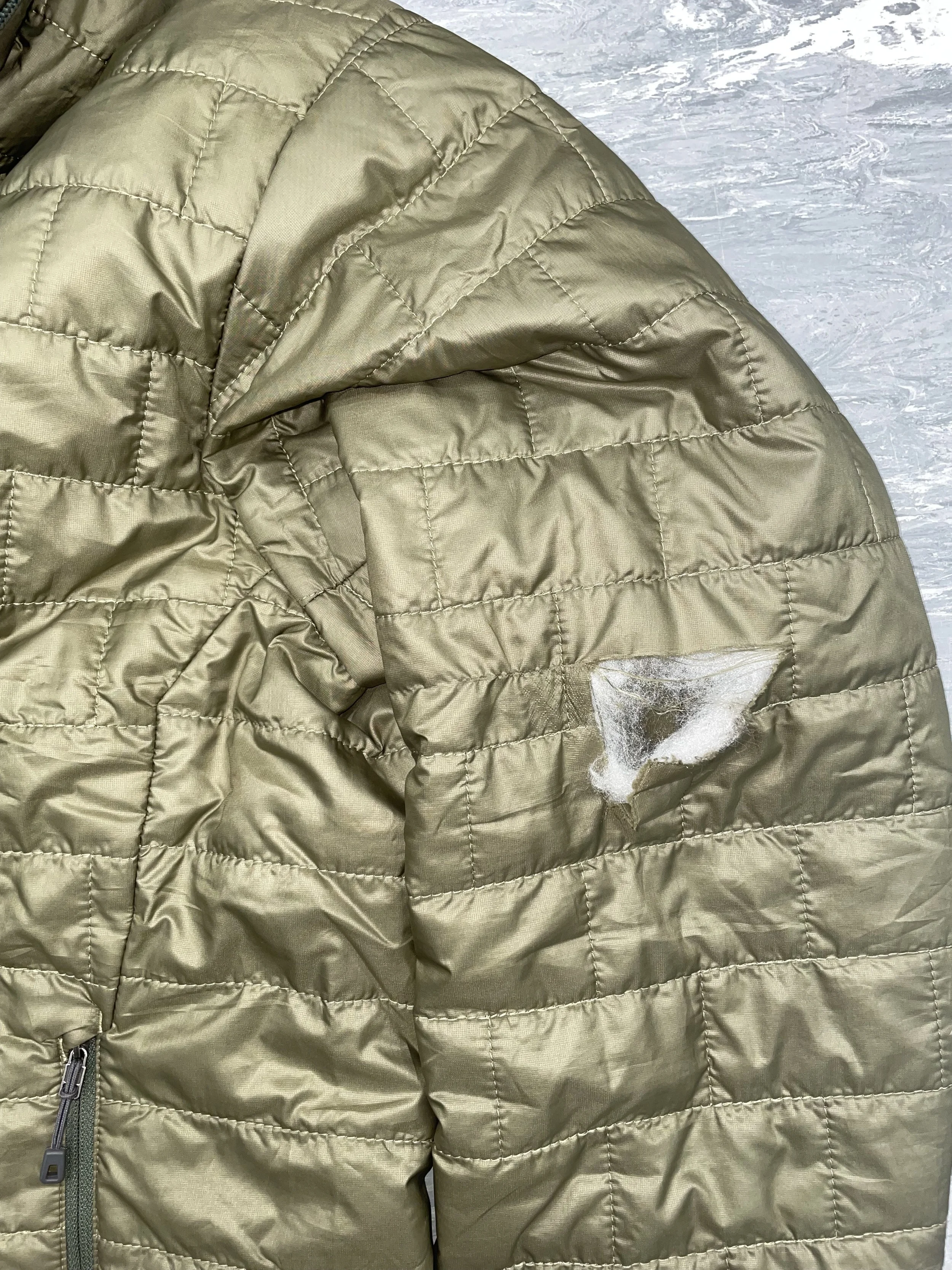 Tear to coat sleeve, affecting both the outer and insulation layers of fabric