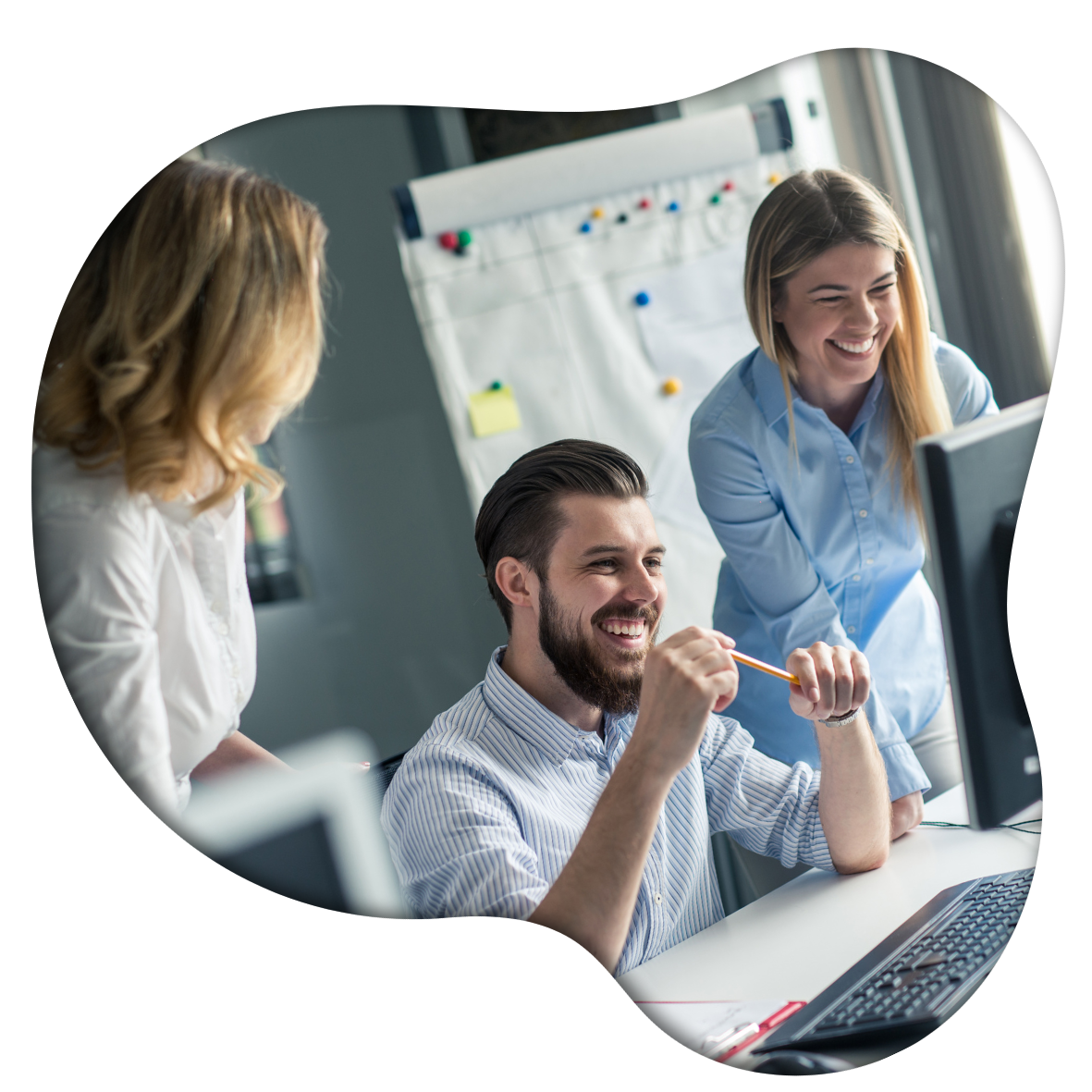 Three colleagues working together in a modern office, smiling and collaborating around a computer, with a whiteboard in the background.