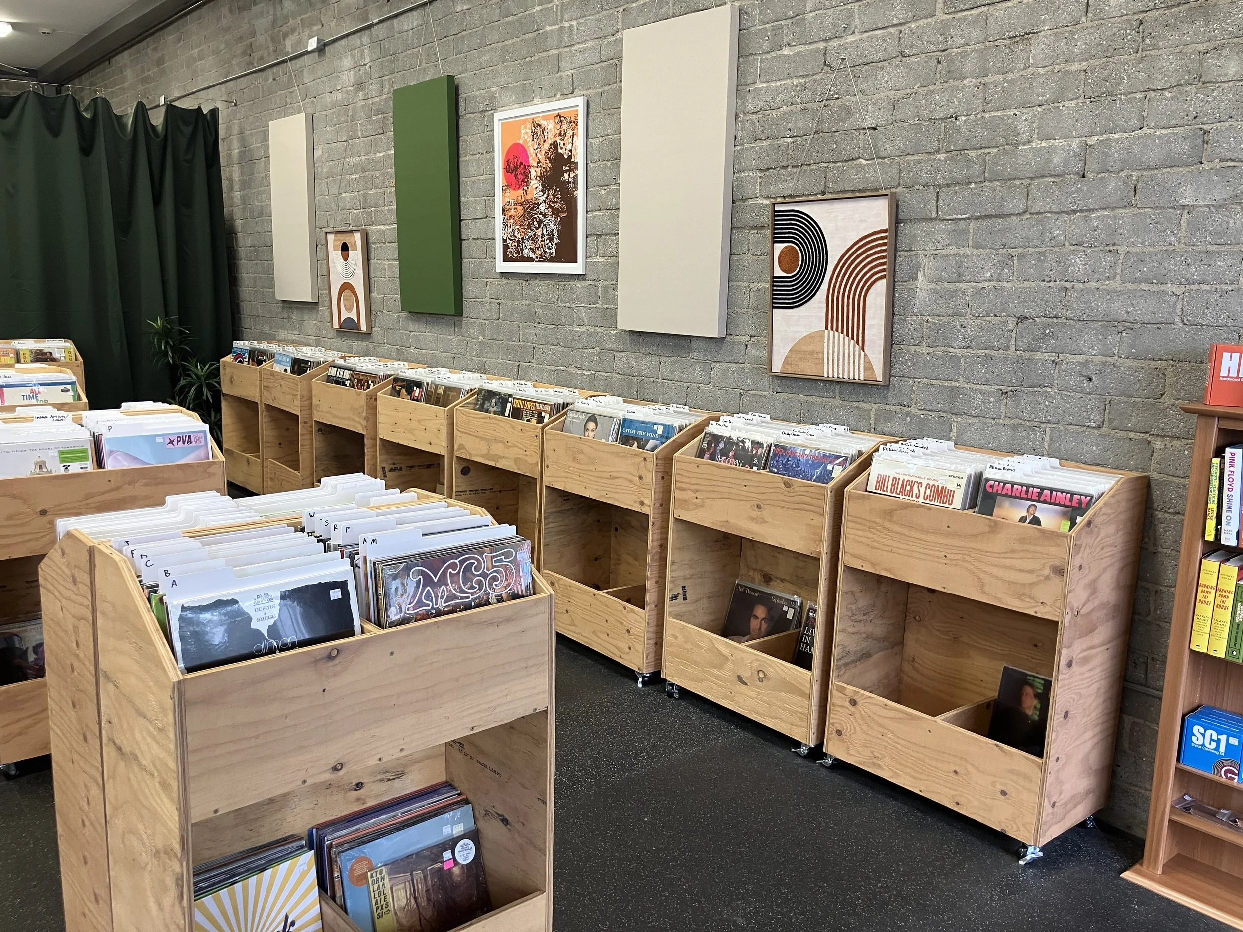 Inside Daystar Records in Burbank, California. Vinyl records fill attractive wooden bins aligned beautifully against an exposed gray brick wall with sound panels and colorful, comforting wall art.