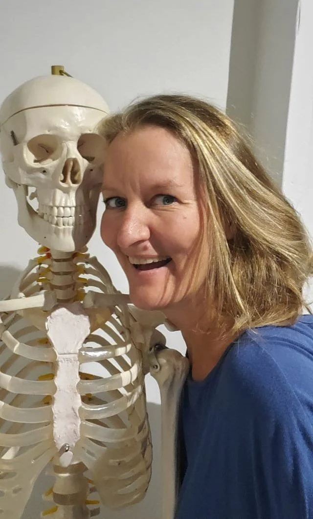 Eine Frau macht ein Selfie neben einem menschlichen Skelettmodell. Die Frau hat blonde Haare und trägt eine blaue Kleidung.