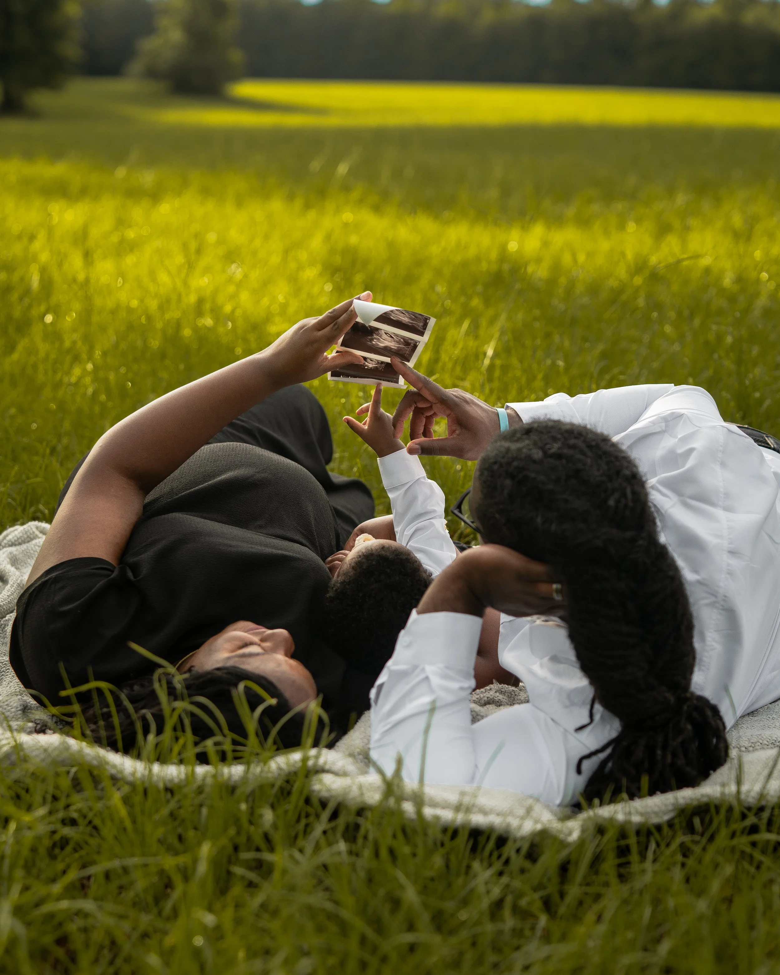 Family lying on blanket in a grassy field, with the mother and child looking at ultrasound images near Hamilton, Alabama