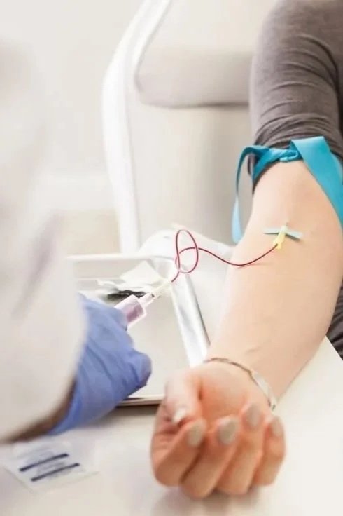 A person donating blood, with a healthcare professional preparing to draw blood from their arm using a needle and tubing.