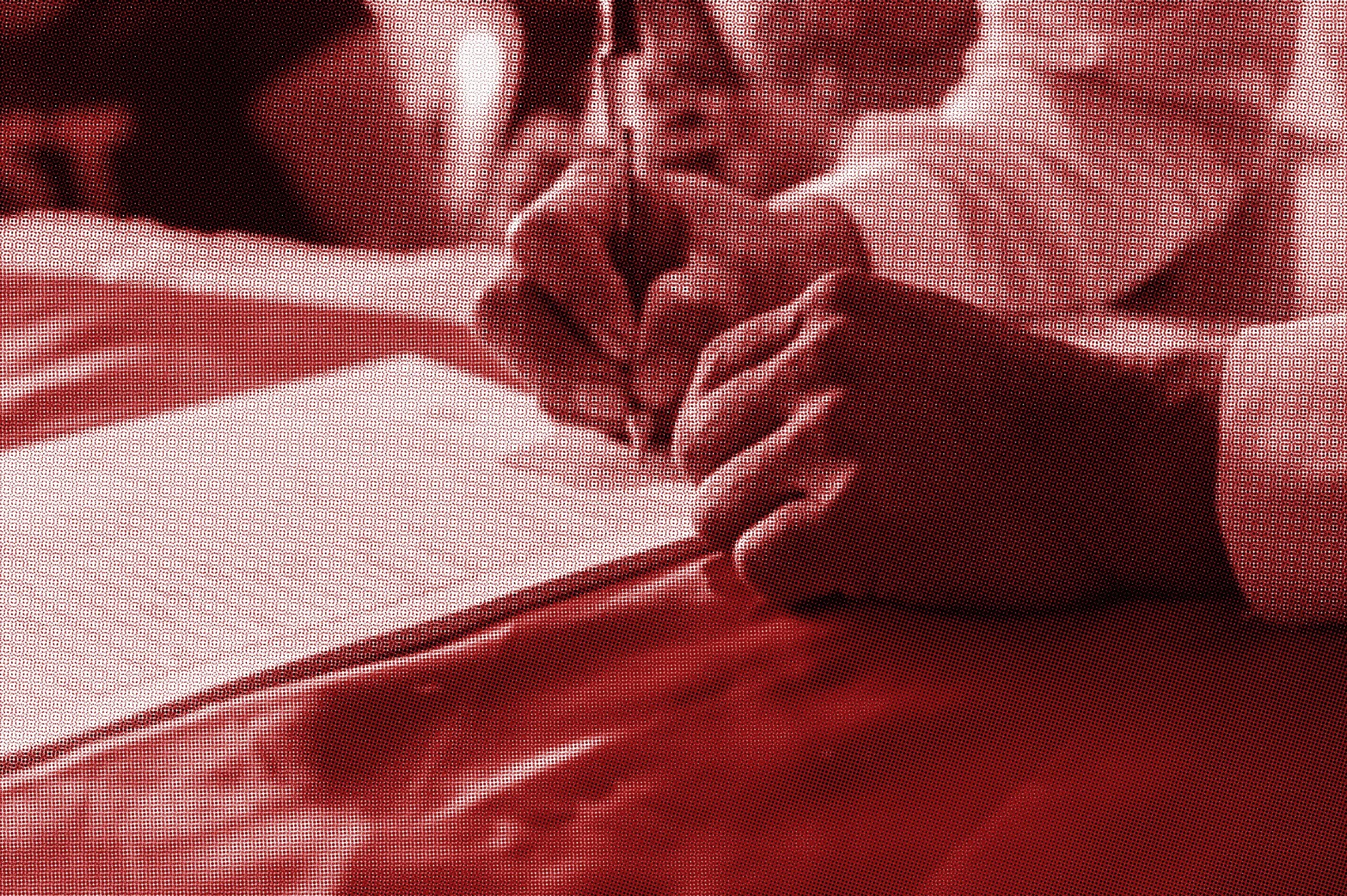 A child is drawing in a notebook with a pencil, holding it with their right hand. The image is tinted red.