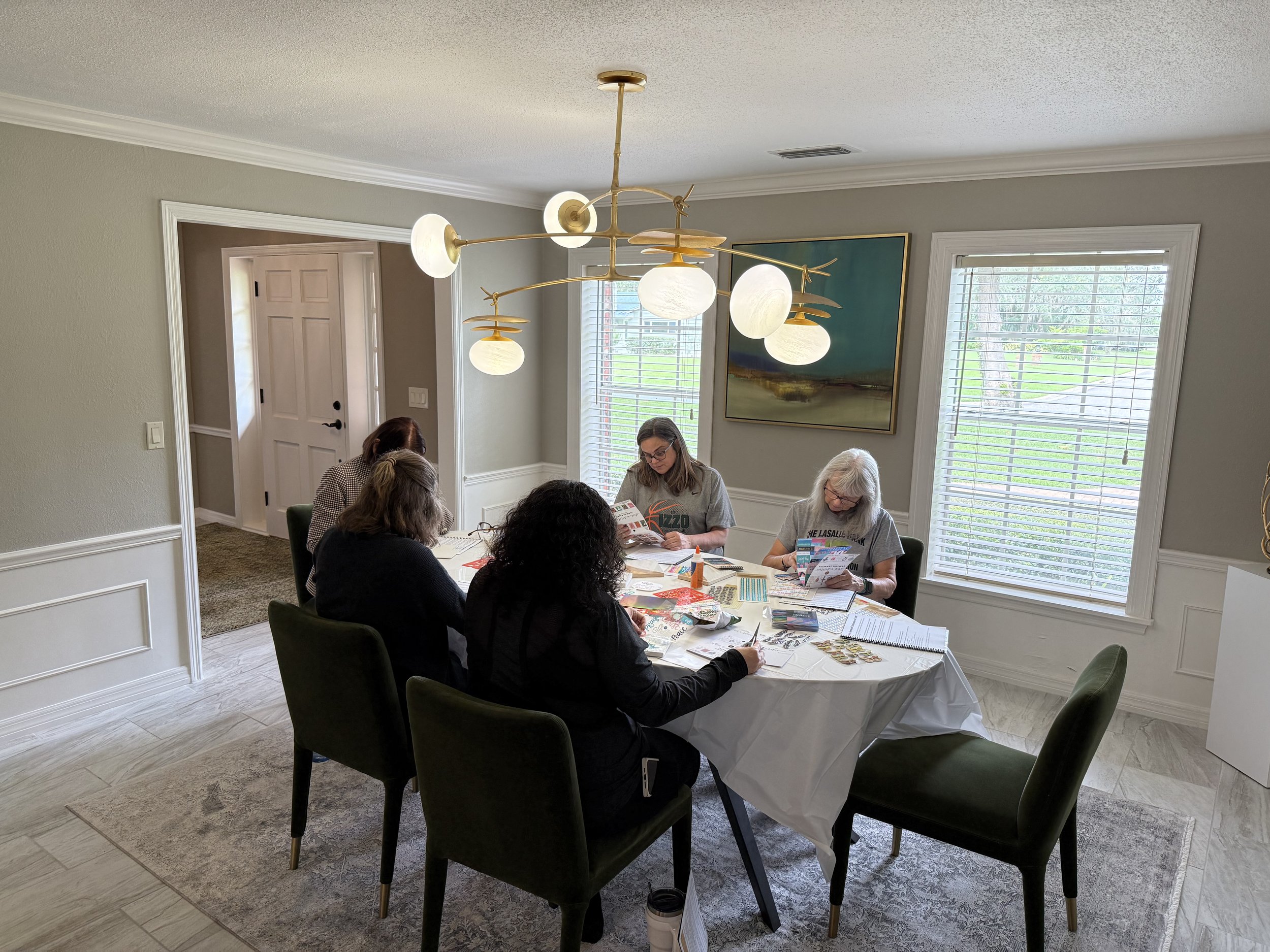 People sitting around a table with papers and magazines, engaging in a group activity in a well-lit dining area with large windows.