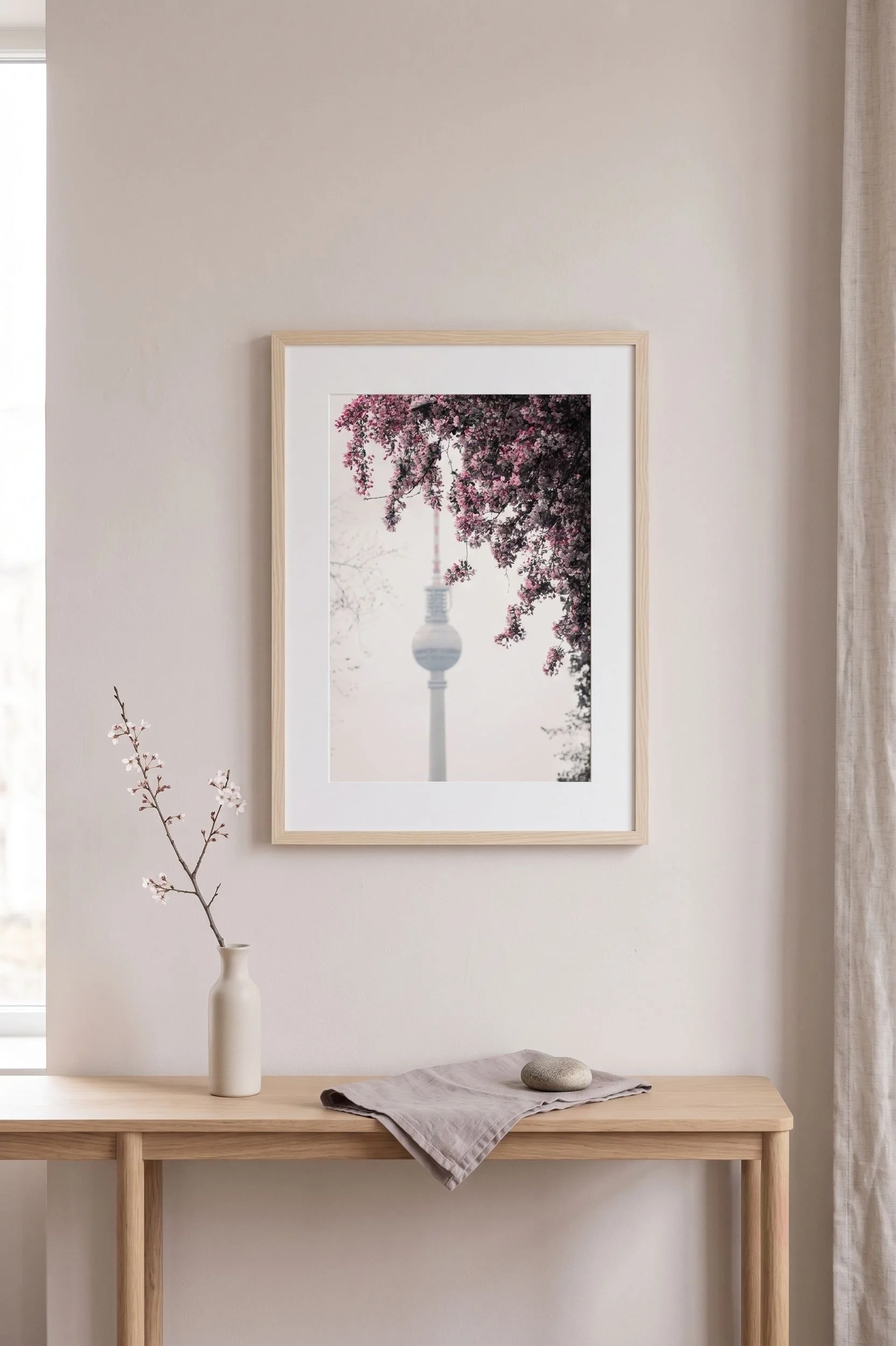 Framed cherry blossom and Fernsehturm print above a light oak console in a Scandinavian living room.