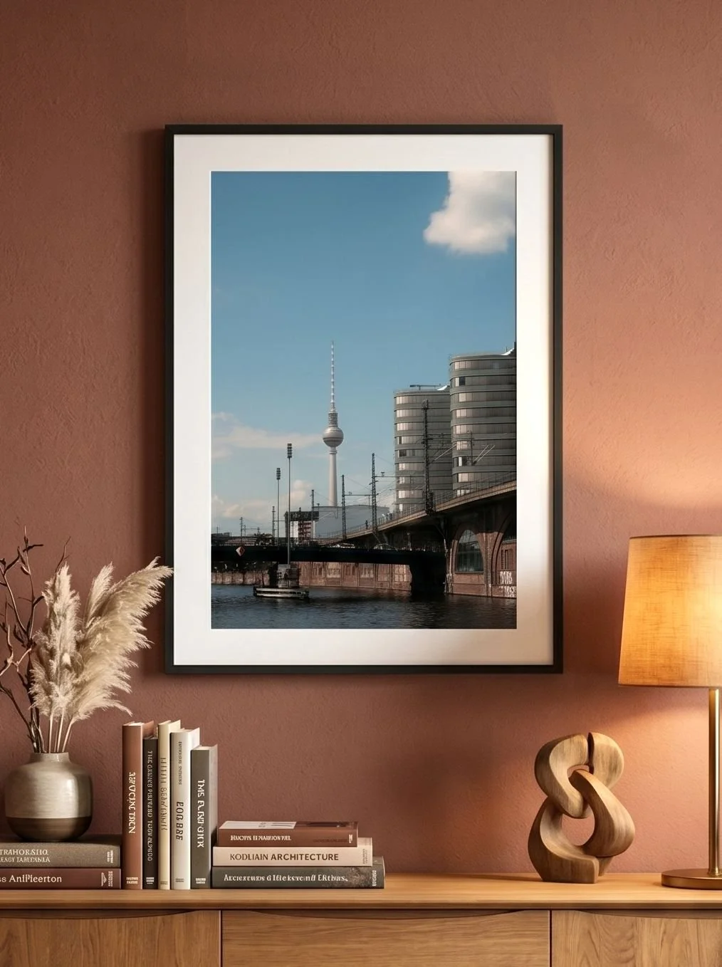 Framed Fernsehturm and Spree print on a terracotta wall above a green leather chair.