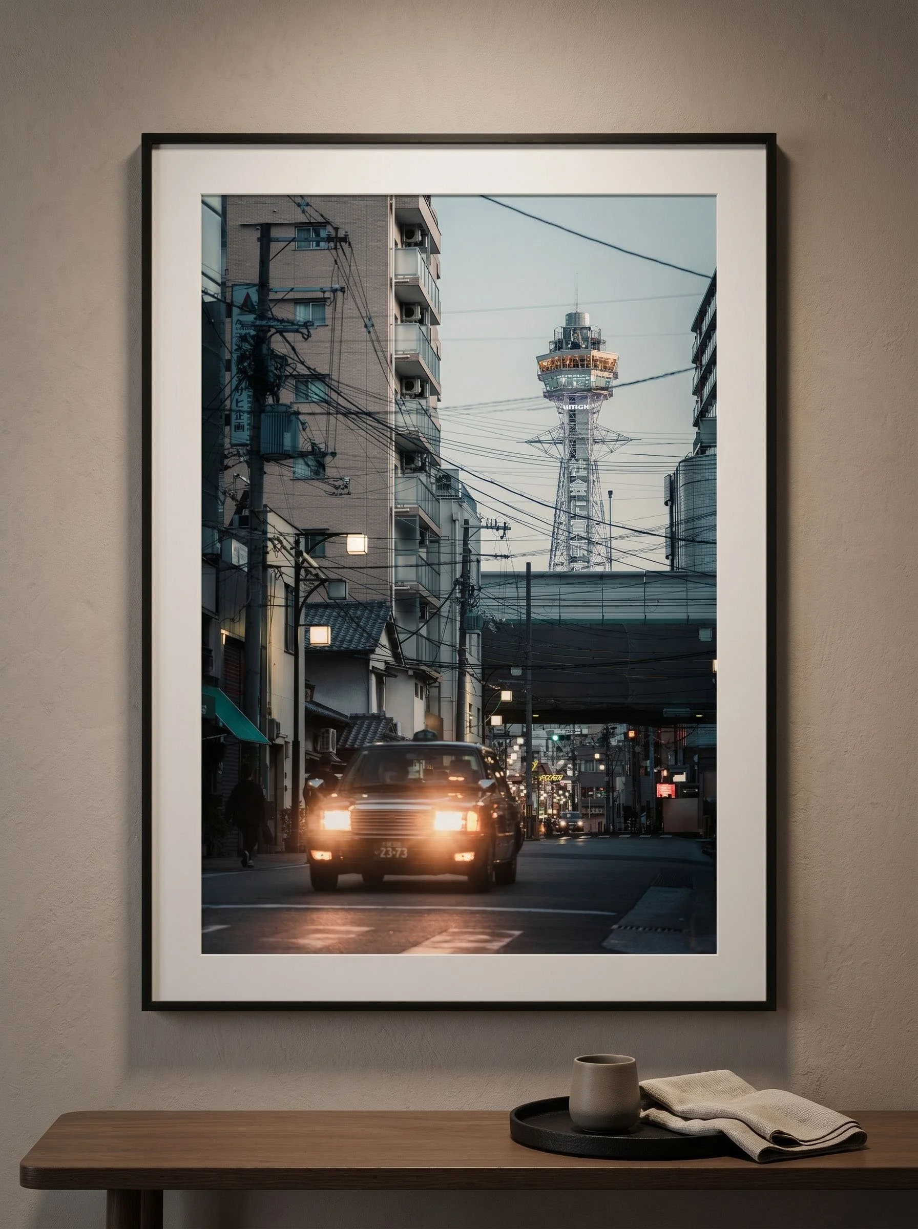 Osaka taxi and Tsutenkaku print in a landscape frame above a warm wood console.