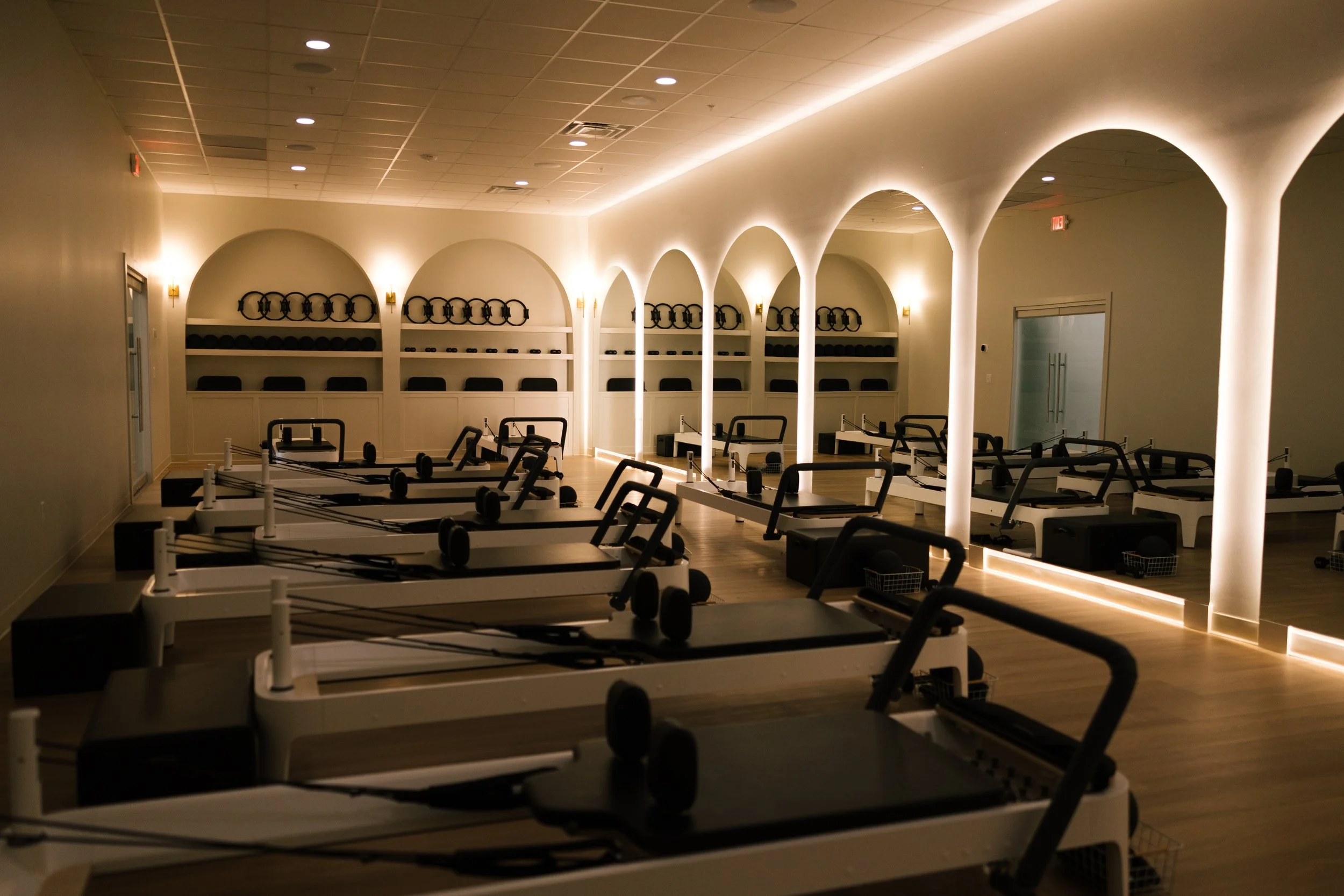 Reformer Pilates machines in a dimly lit fitness studio with arched wall features and soft lighting.