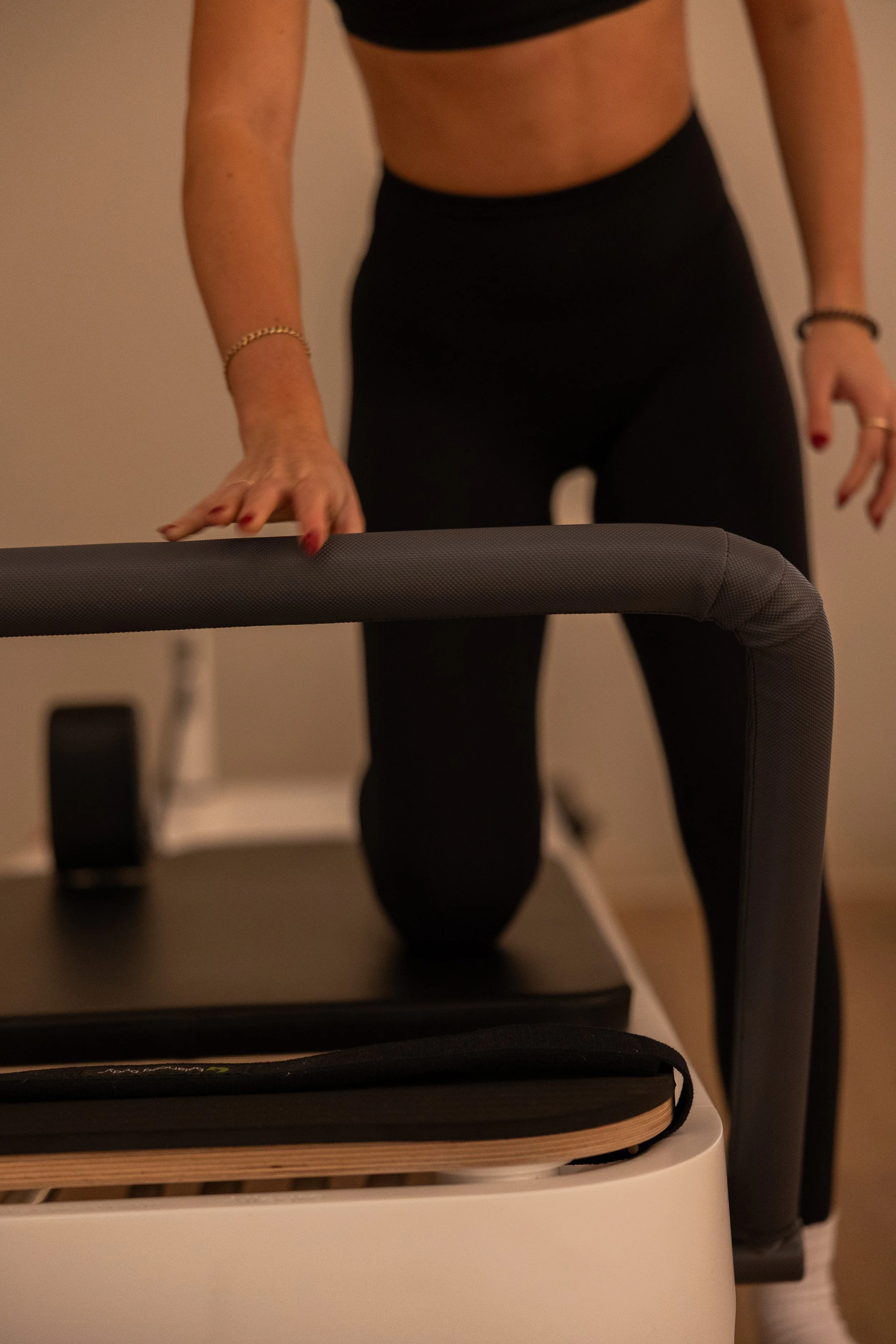 Person in black workout clothes standing on a treadmill, with one hand resting on a rail and the other hanging by their side.