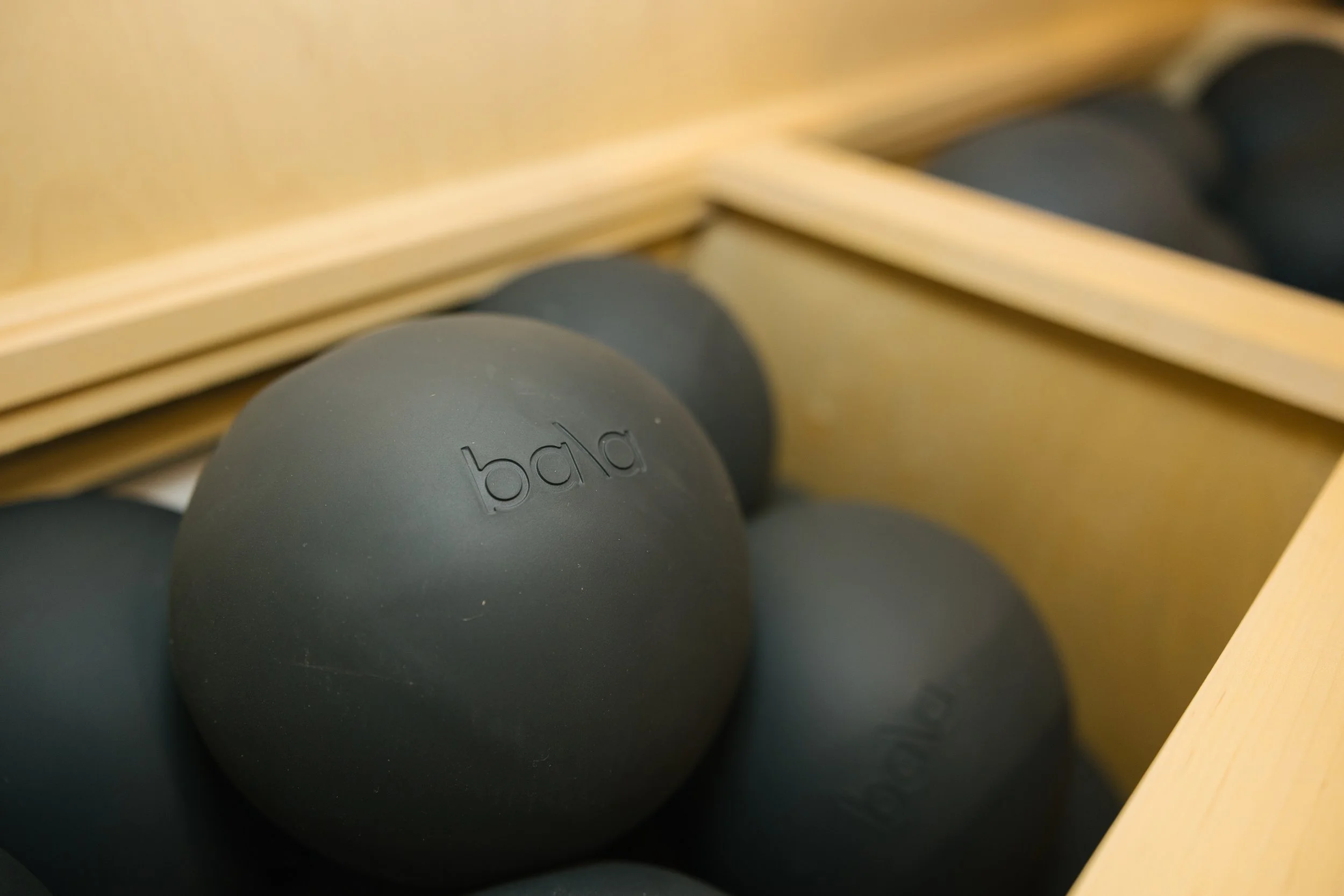 Black massage balls in a wooden box, with the word 'bala' engraved on one of them.