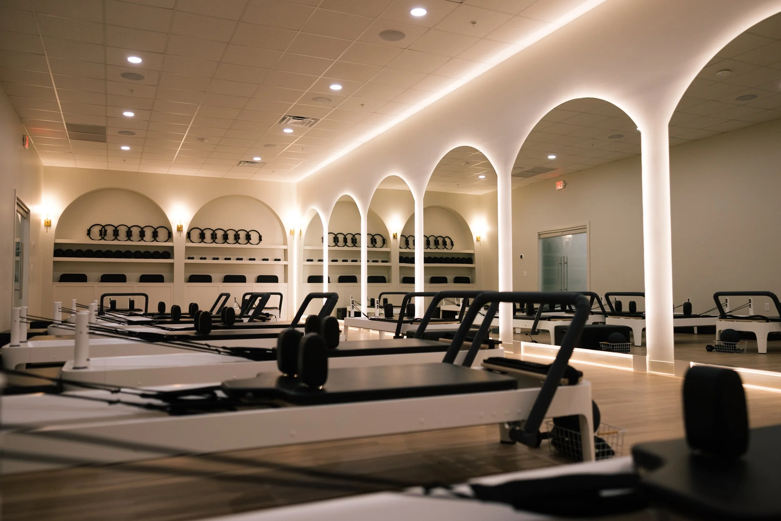 Empty Pilates reformer mats and equipment in a modern fitness studio with white walls and soft lighting.