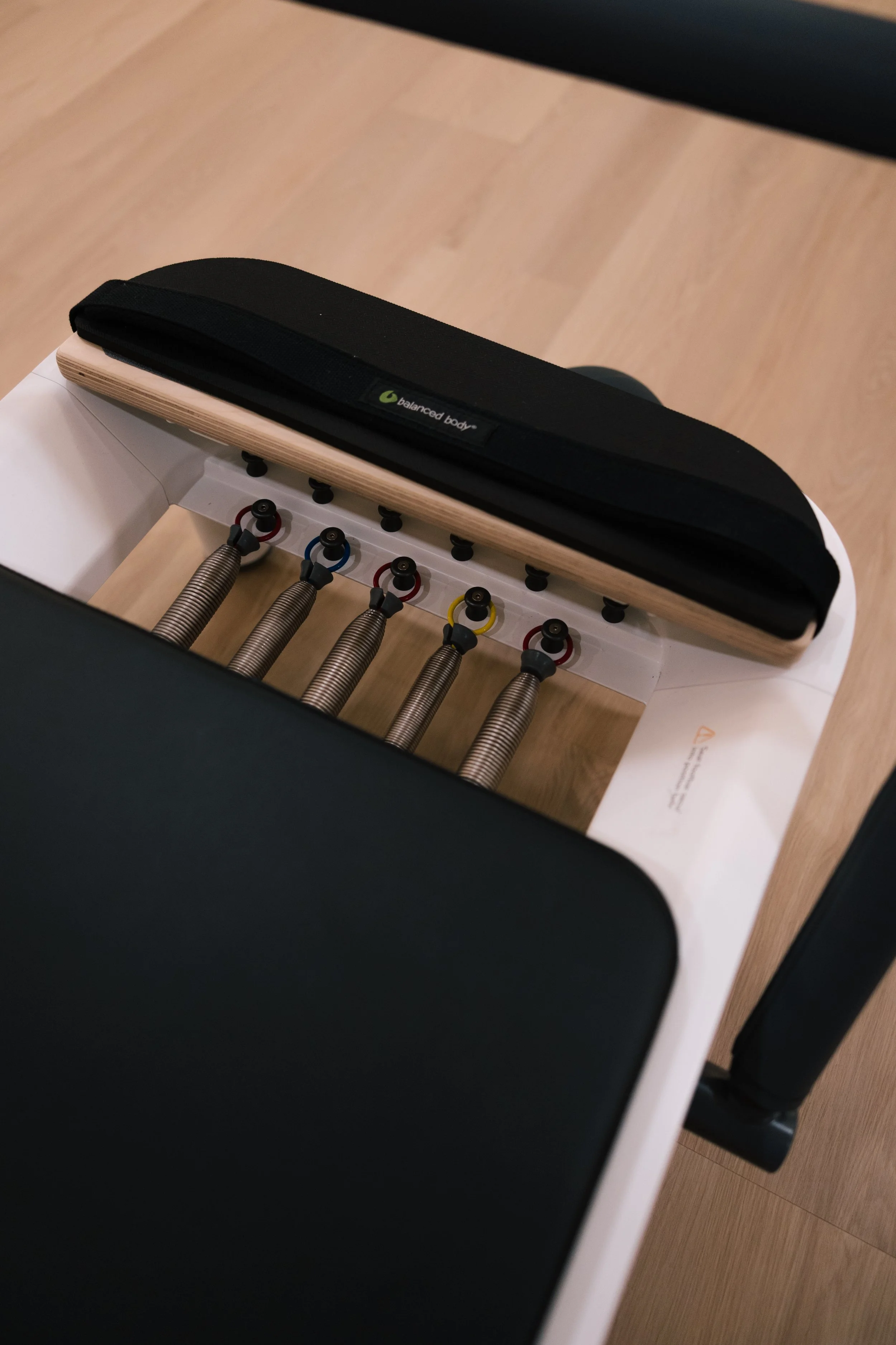 Physical therapy or exercise apparatus with five spring-loaded bars, each with different colored rings, on a white table with wooden and black padded surfaces.