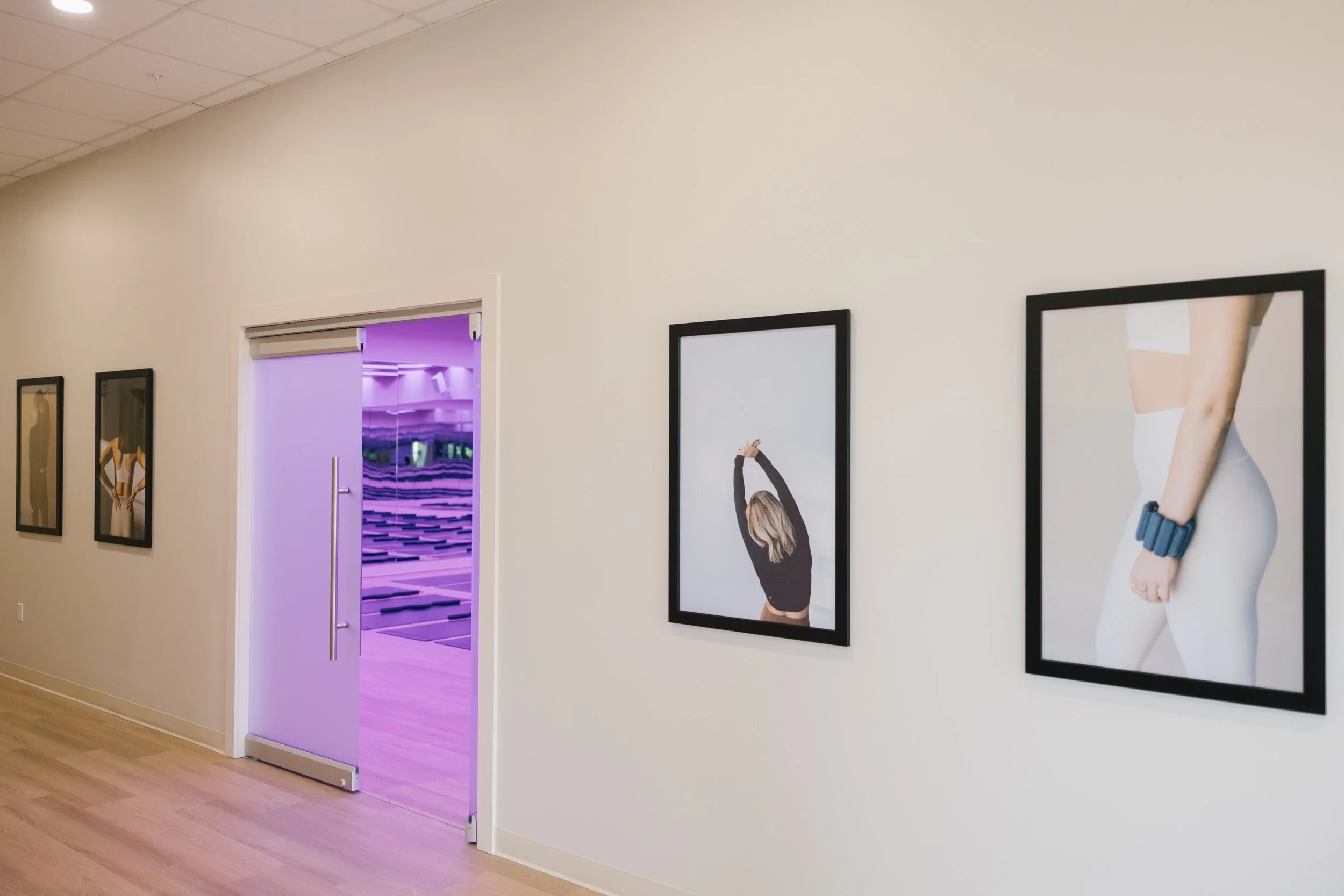 Gallery wall with five framed photographs of women, one with a woman with blonde hair stretching, another with a woman in white activewear with a blue fitness tracker.