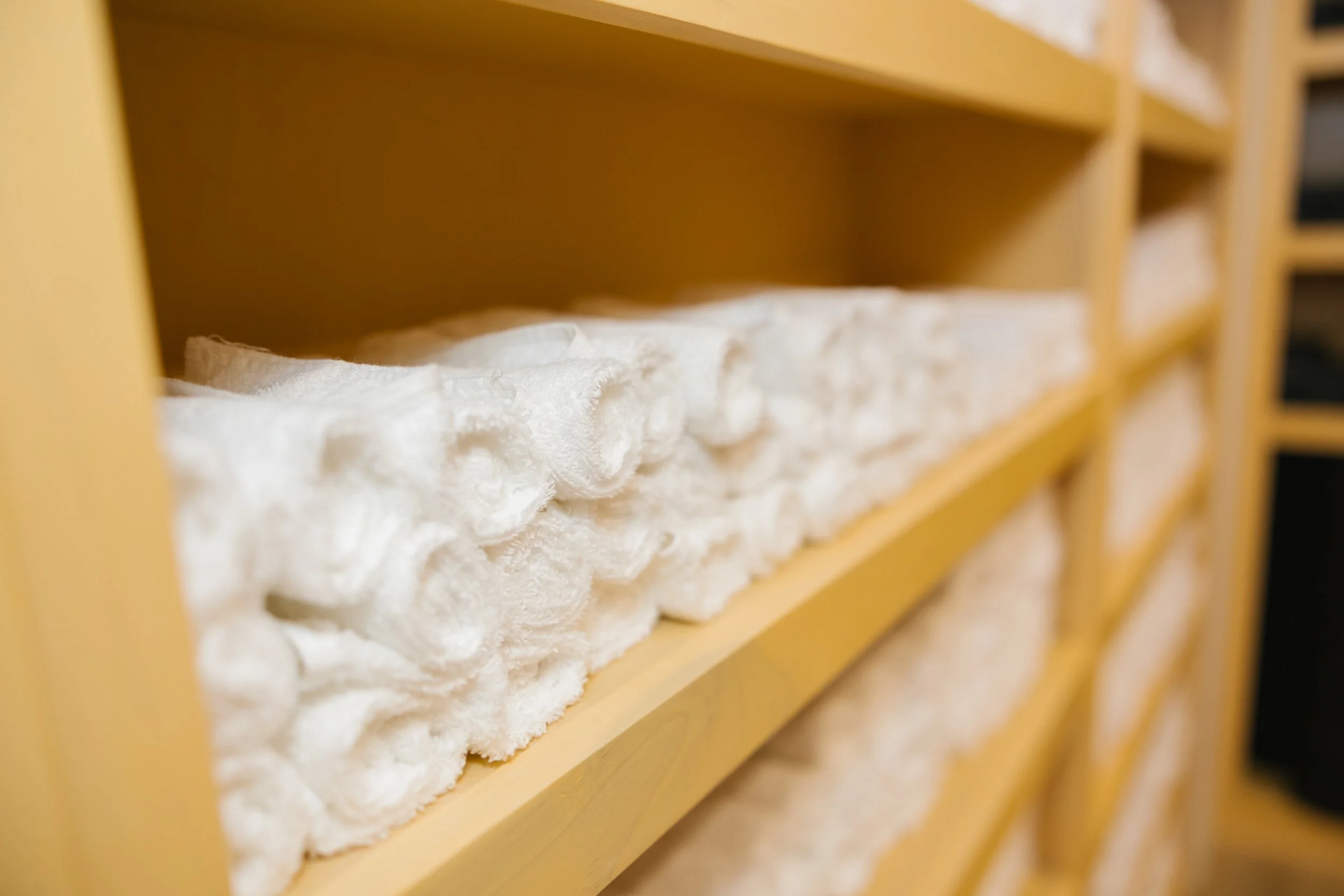 Close-up of neatly folded white towels on wooden shelves in a store or linen closet.
