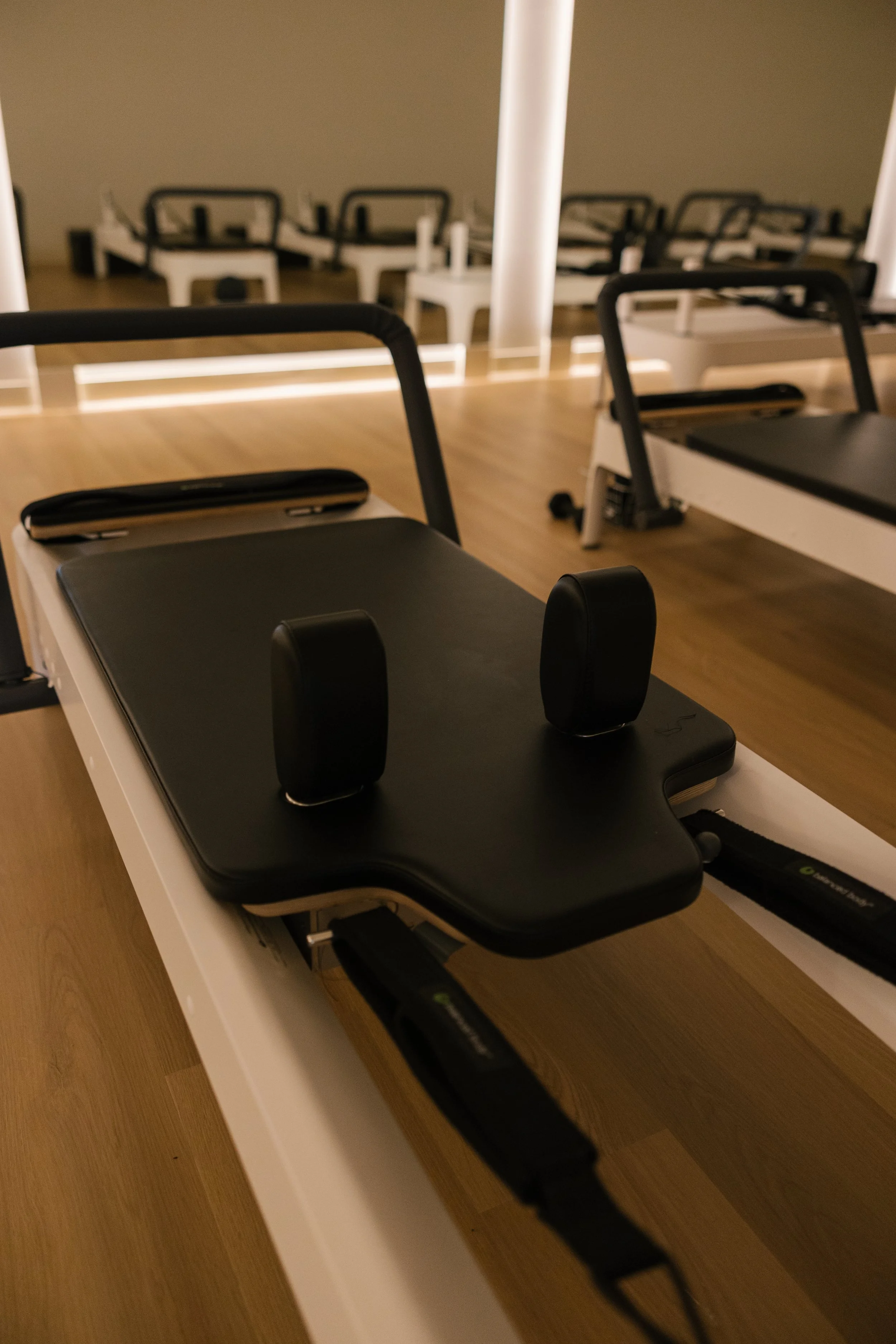 A Pilates reformer machine in a gym with wood flooring and multiple other reformers in the background.