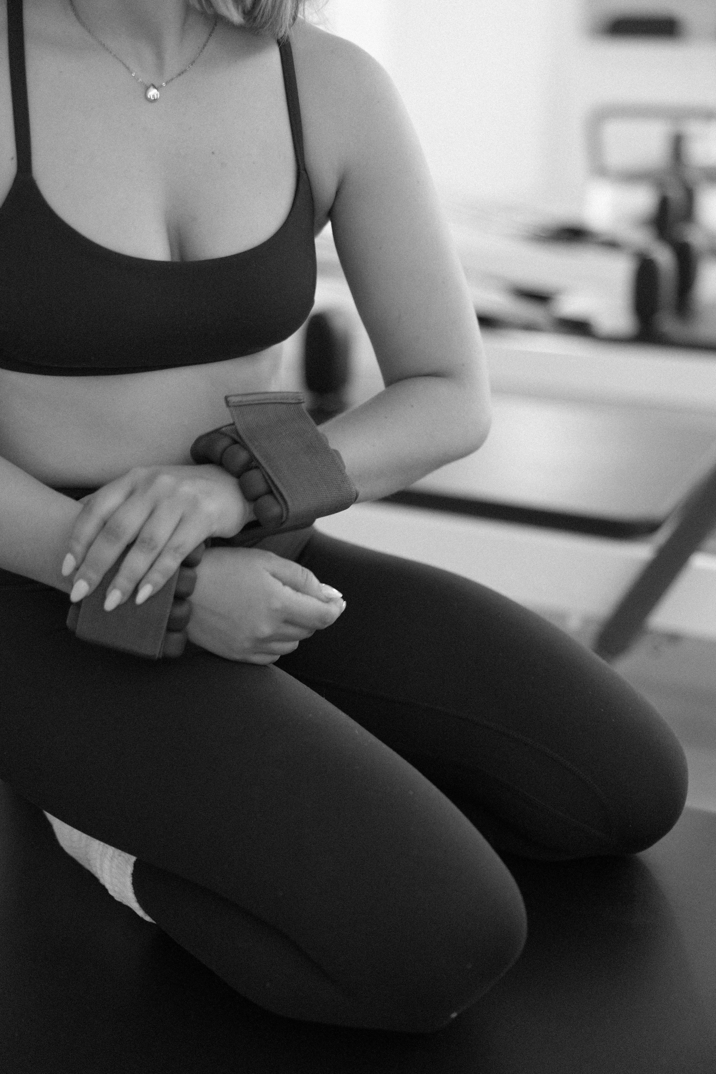 A woman kneeling on the floor in a gym, wearing a sports bra, leggings, and hand wraps, with her hands resting on her lap.