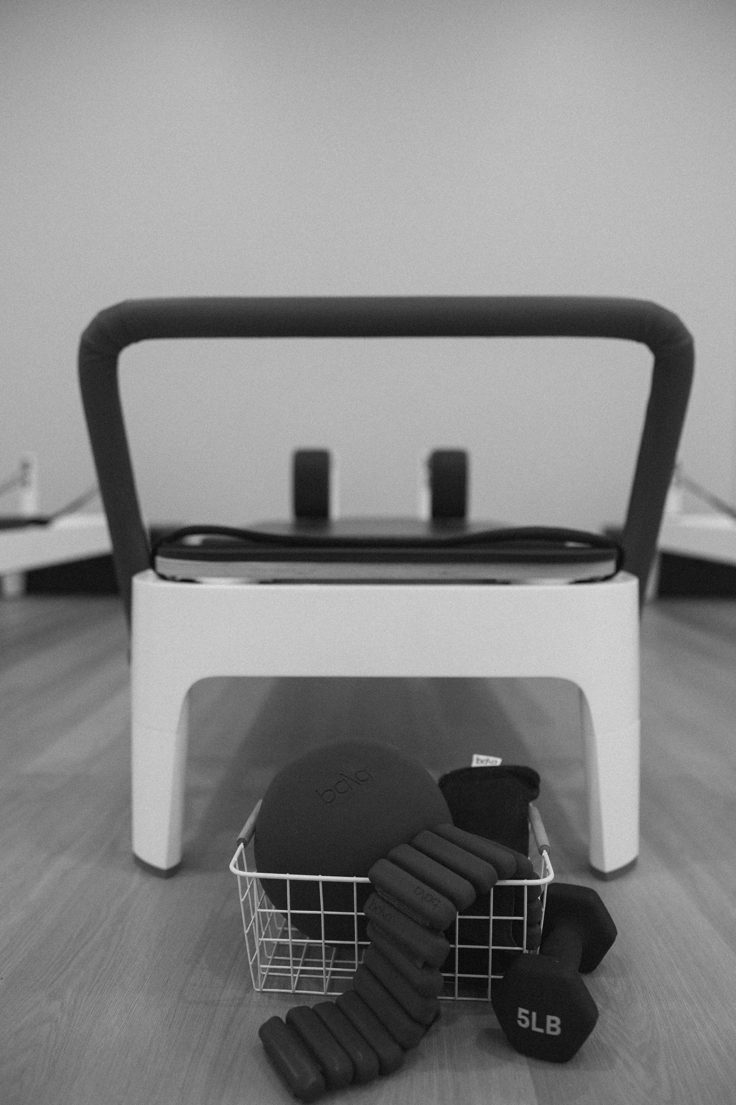 Workout equipment including a kettlebell, a resistance band, and a dumbbell, placed under a small chair in an indoor setting.