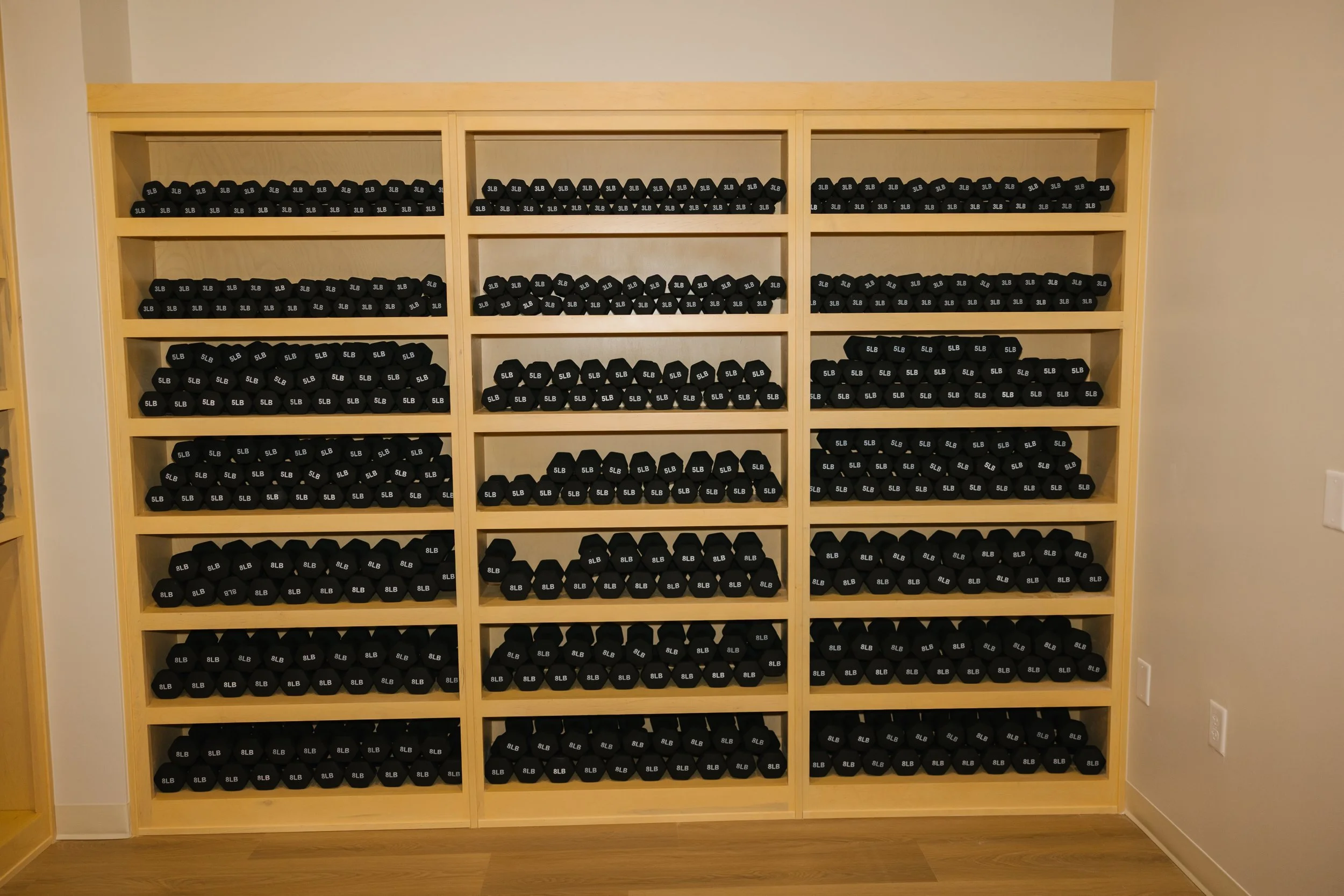 Wooden shelves filled with black 5-pound dumbbells labeled '5LB'
