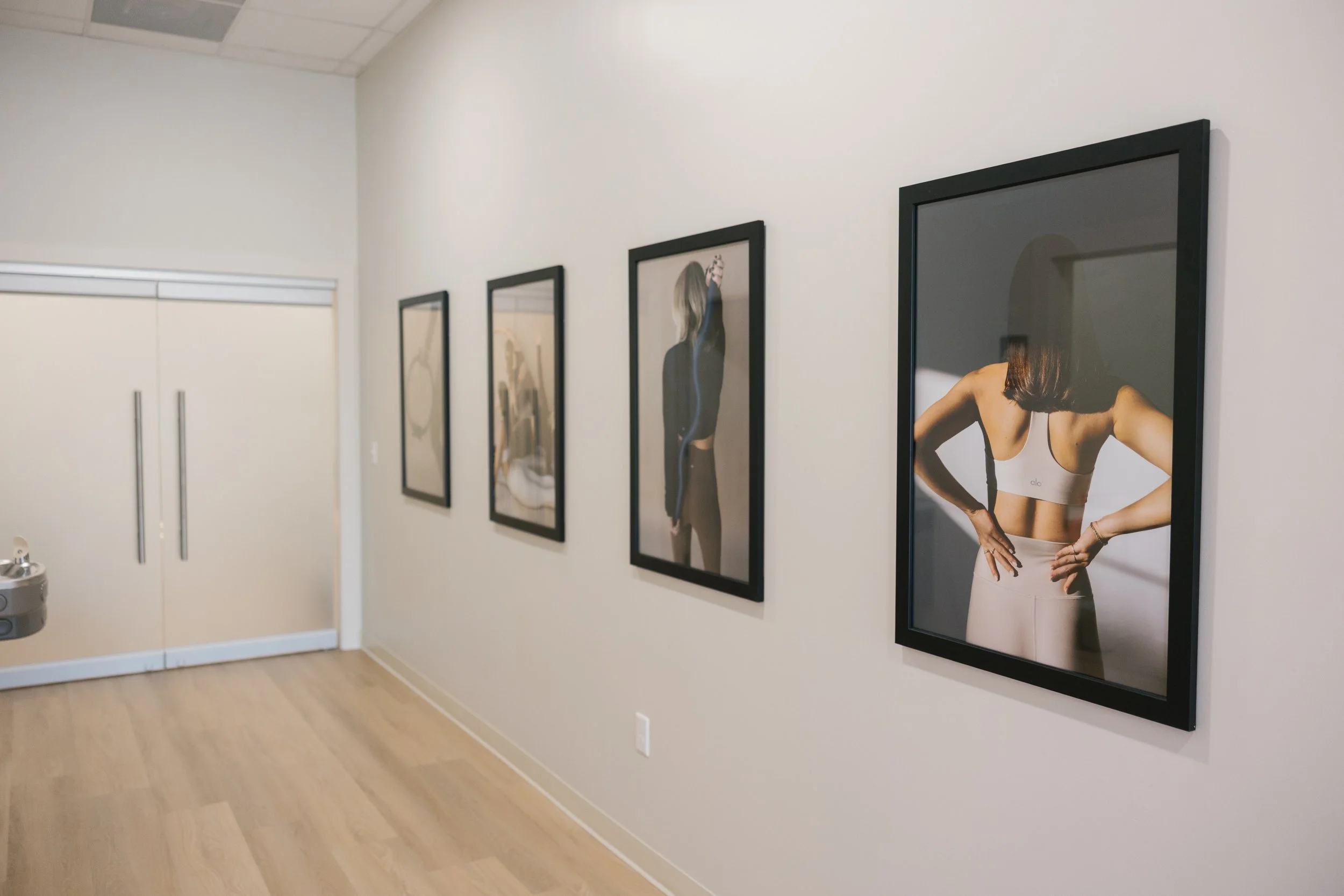 Gallery wall with four framed photographs of women in athletic clothing, on a white wall in a room with wooden floors.