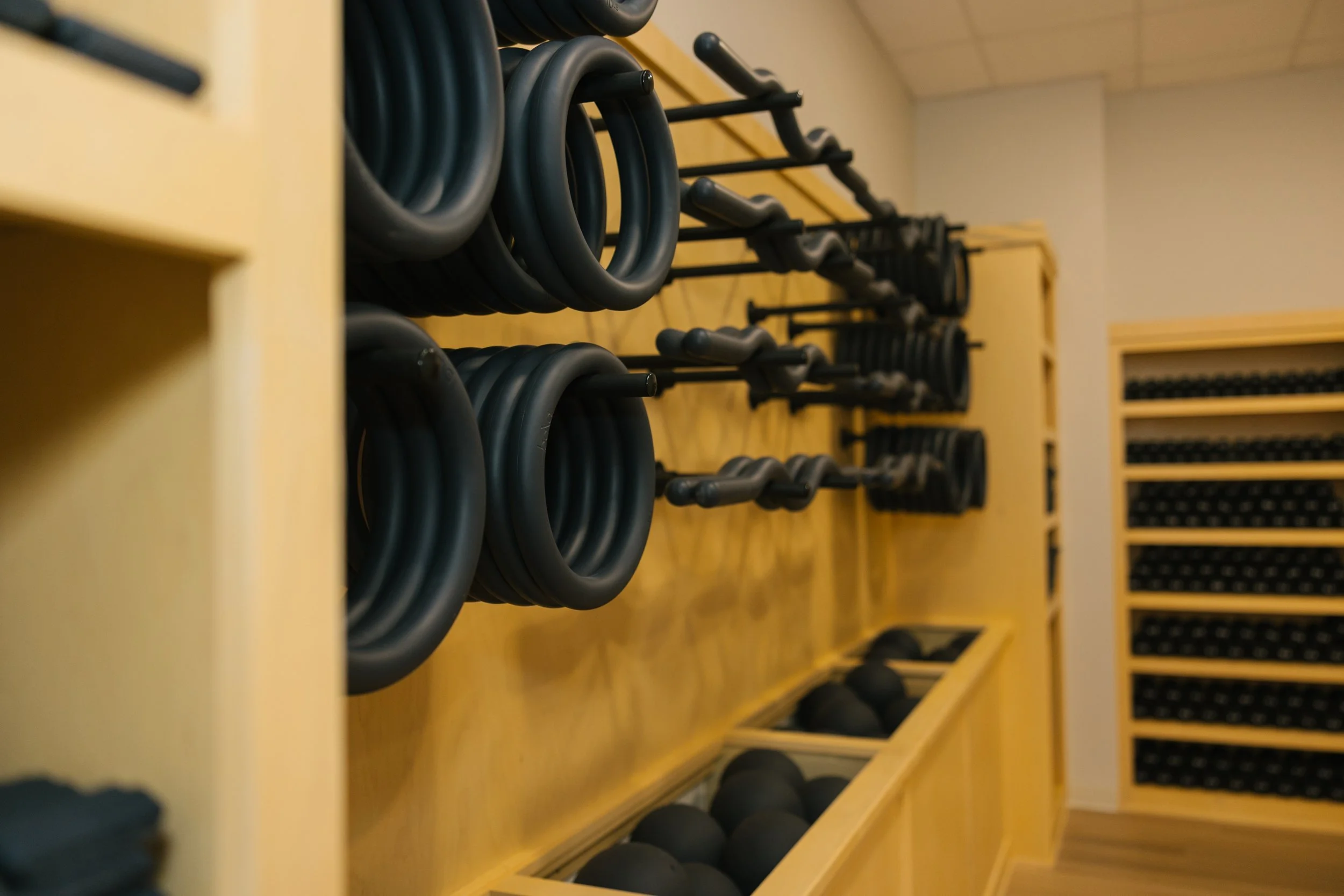 Workout equipment in a gym, including black resistance rings, dumbbells, and medicine balls stored on yellow wooden racks.