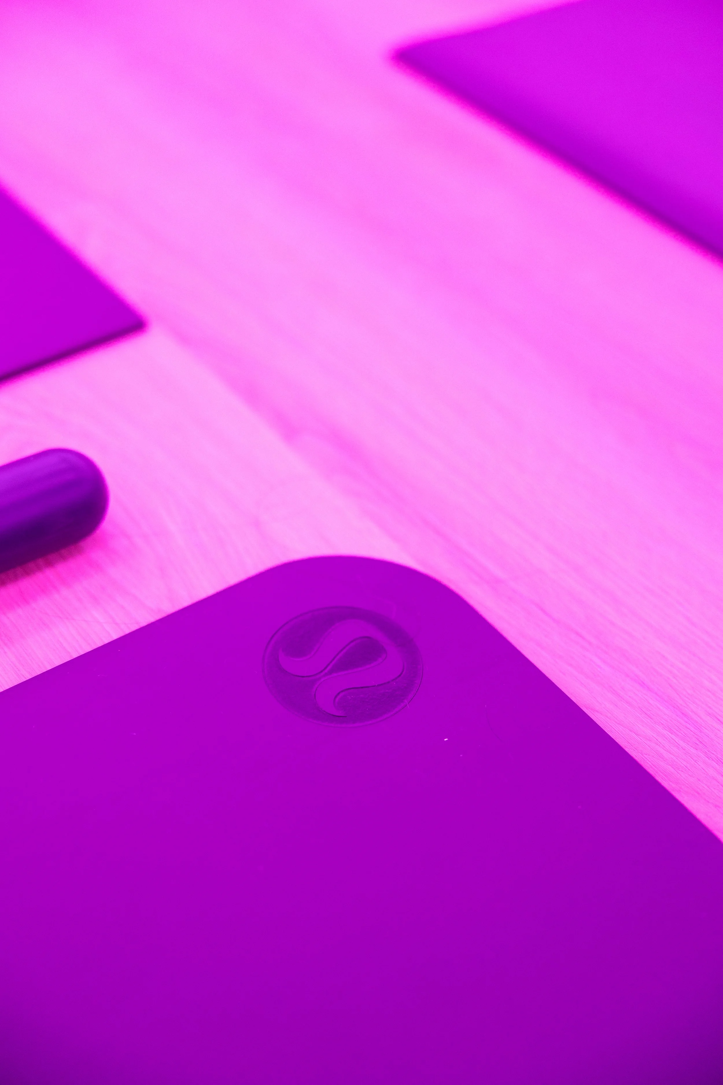 Close-up of a purple desk with a round logo on a device, under pink and purple lighting.