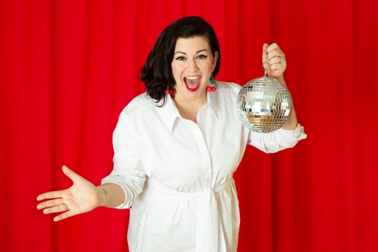 Personal branding coach and Higher Voltage event organiser Christine Gritmon smiling and holding a disco ball in front of a red curtain.