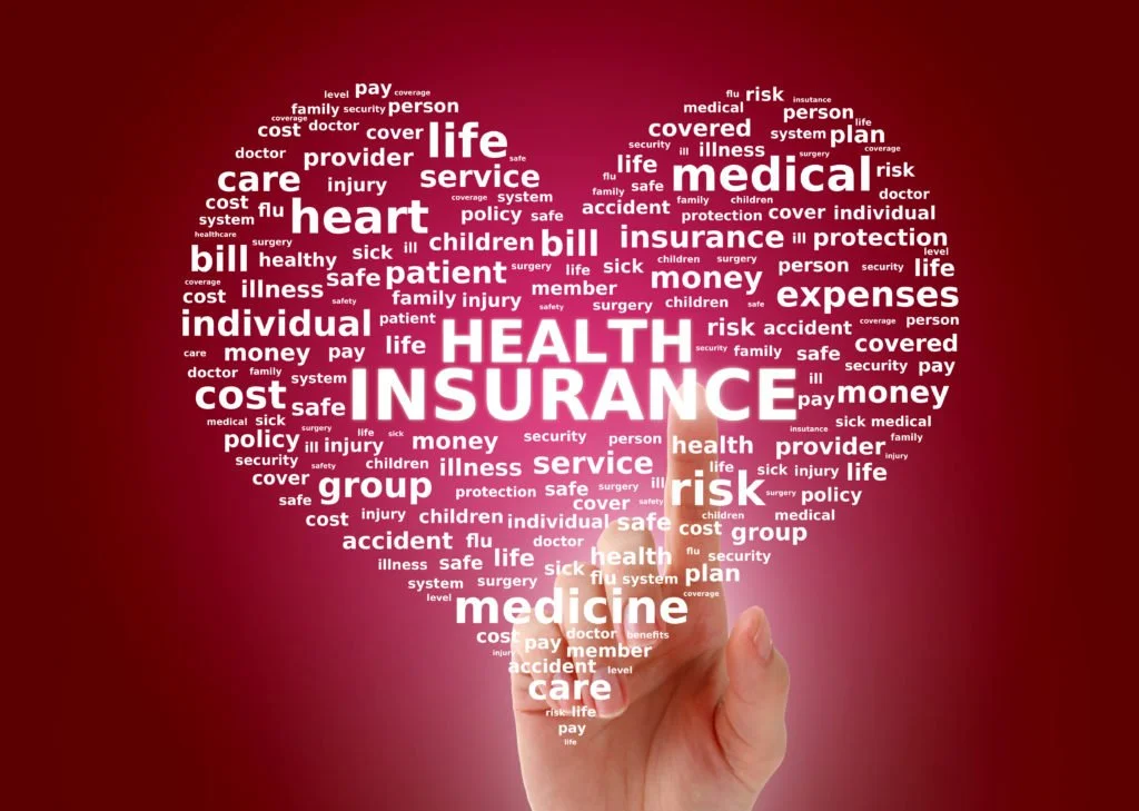 Word cloud in the shape of a heart with terms related to health insurance, medicine, healthcare, and medical expenses on a pink background, with a hand holding a marker at the bottom.