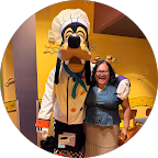 Person standing next to a mascot dressed as Pluto in a Disney theme park