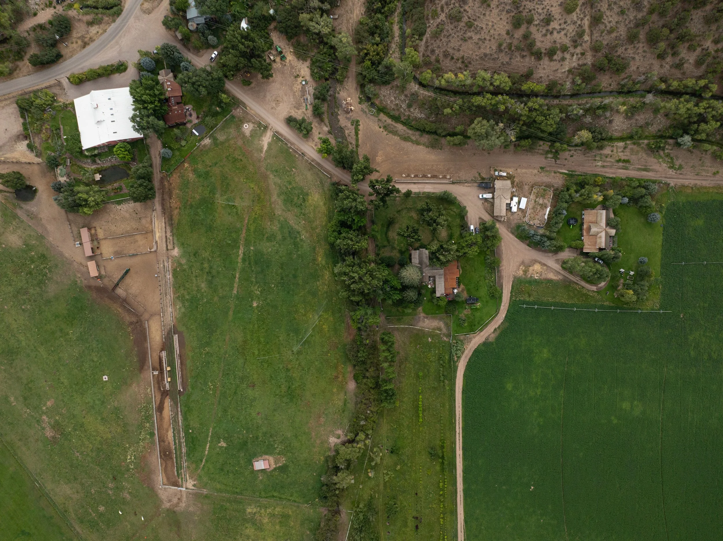An aerial view of a rural area showing houses, green fields, dirt roads, and trees.