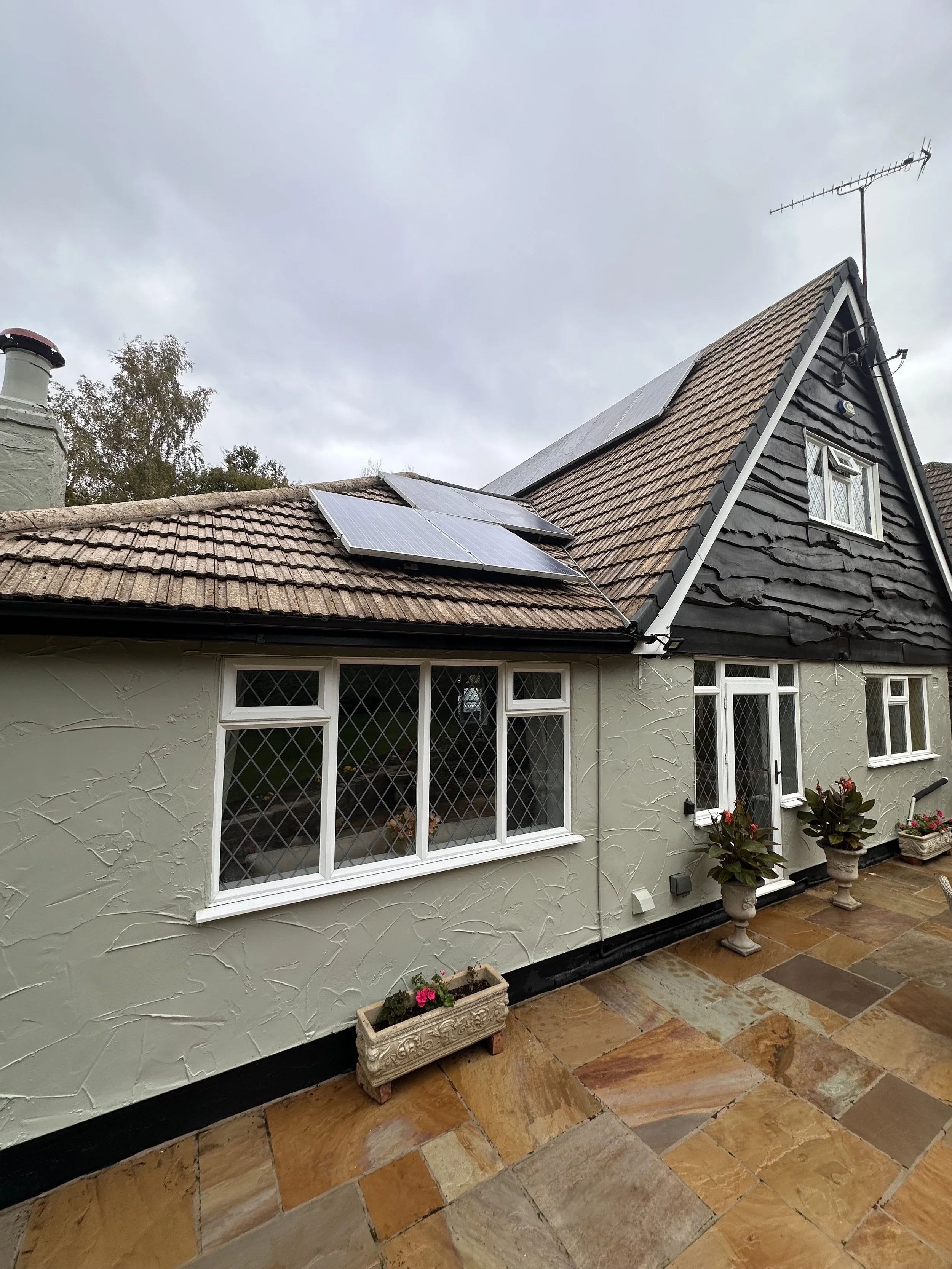 Exterior view of a house with solar panels on the roof, a window with diamond-patterned panes, and decorative flower pots on a stone patio
