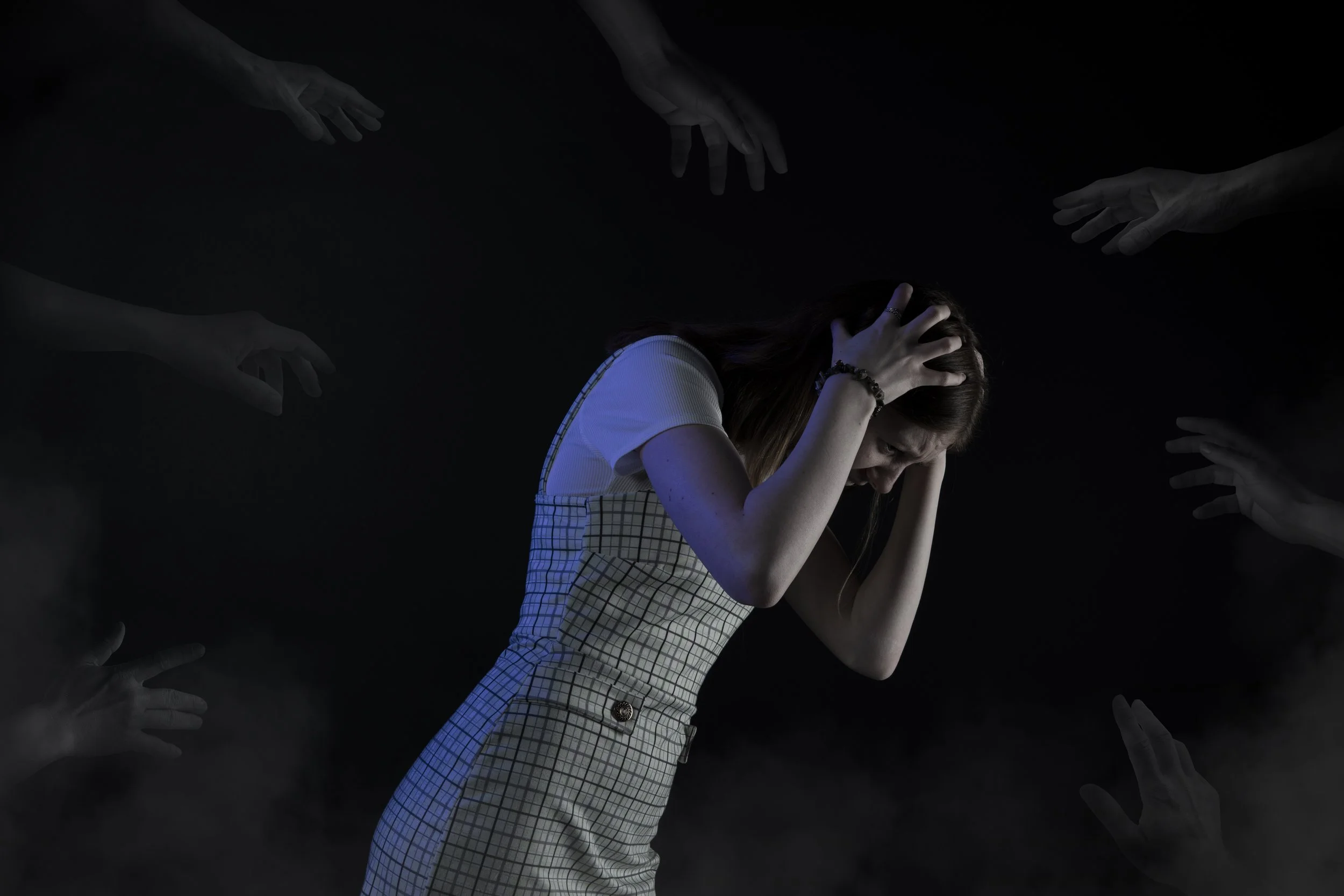 A woman appears distressed, holding her head with her hands, surrounded by ghostly floating hands against a dark background.