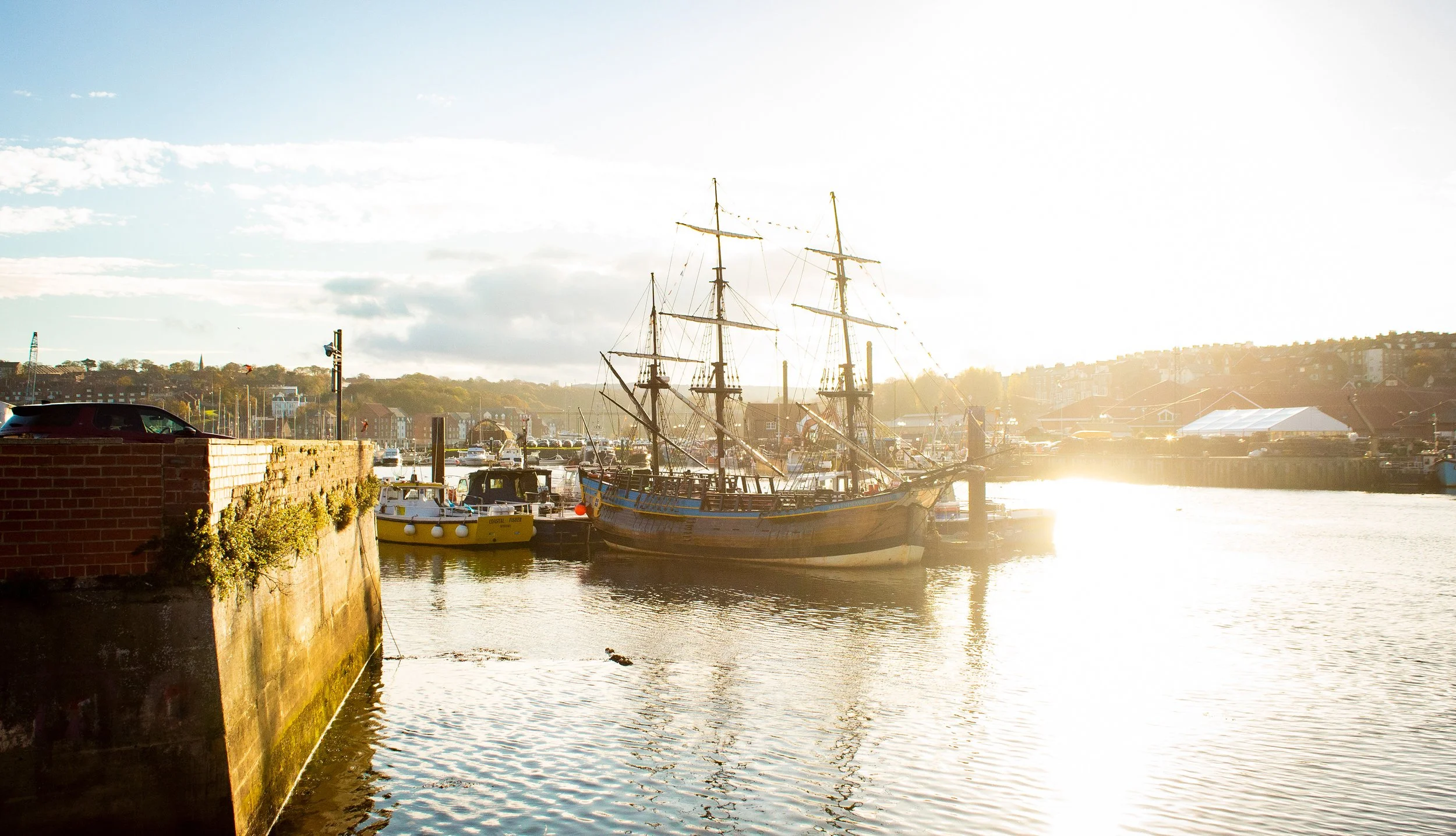 Boats docked at a marina during sunset with a brick pier and a clear sky.