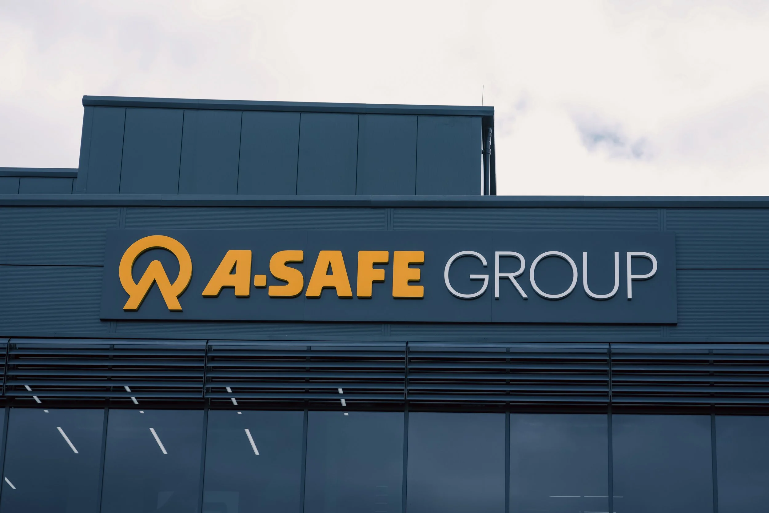 Sign on a building reads 'A-SAFE GROUP' with a logo, part of a modern building with blue exterior walls and tinted windows.