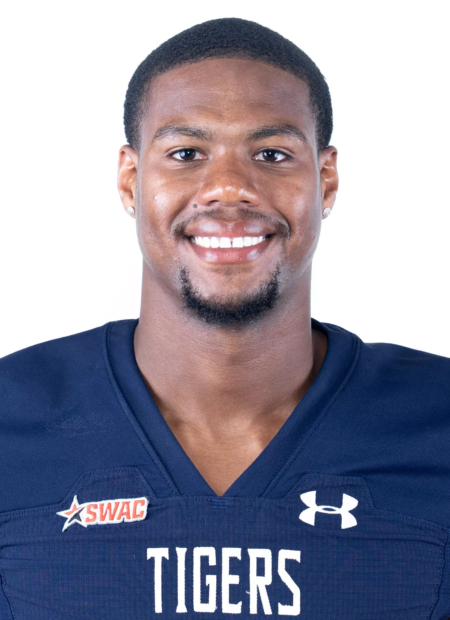 Portrait of a young African American male athlete smiling, wearing a navy blue football jersey with 'TIGERS' written on it, and logos 'SWAC' and Under Armour.