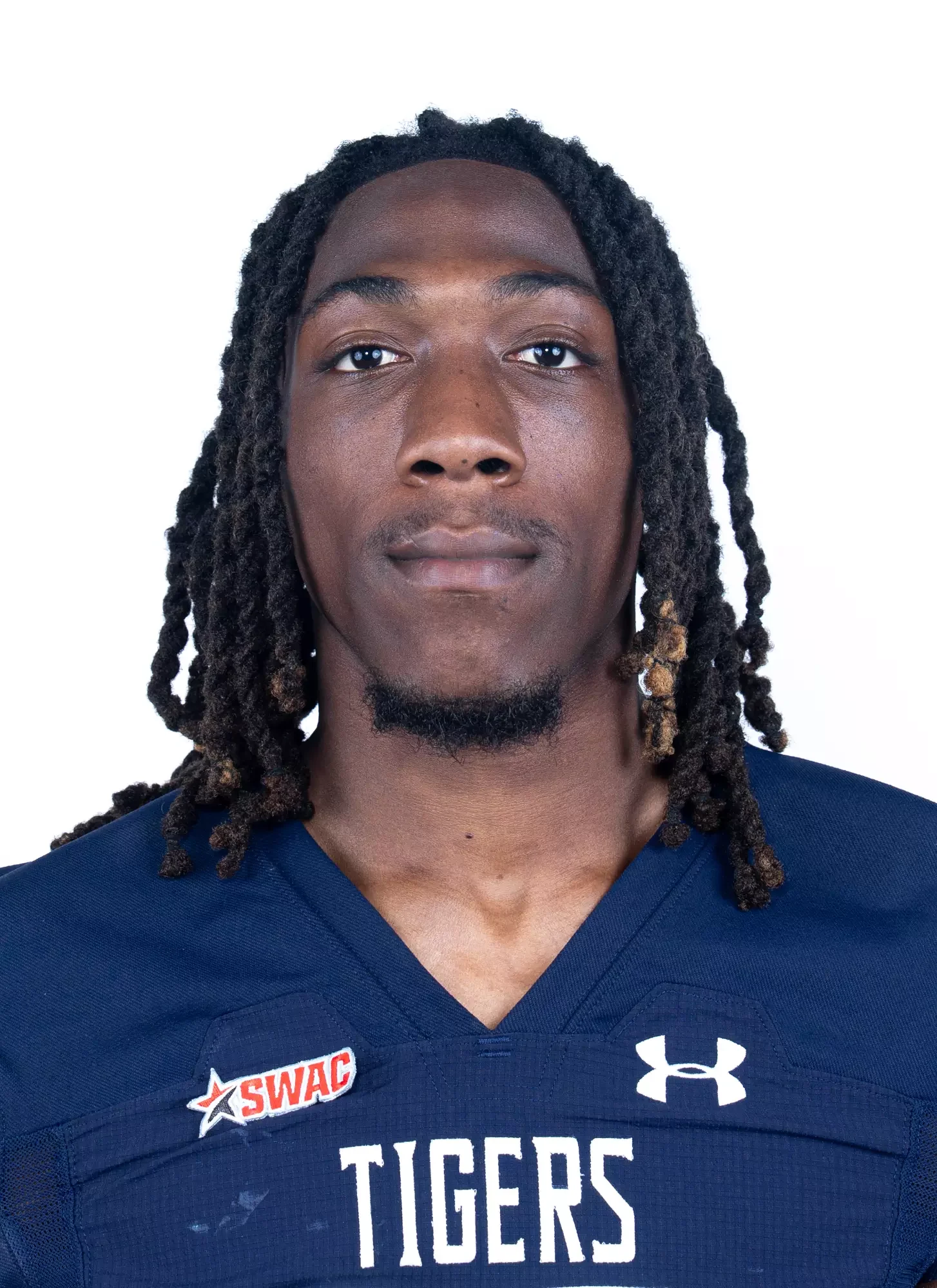 Close-up portrait of an African American male football player wearing a navy blue jersey with 'TIGERS' and patches, against a plain white background.