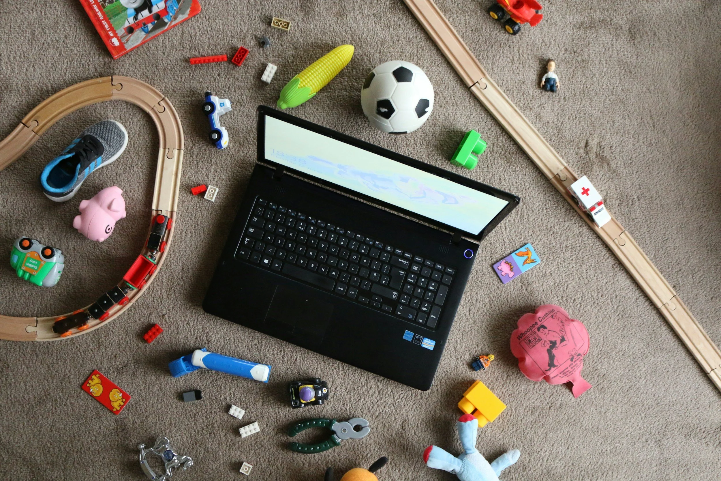A laptop is surrounded by a mess of toys. It represents the chaos and overwhelm caused by being a working parent.