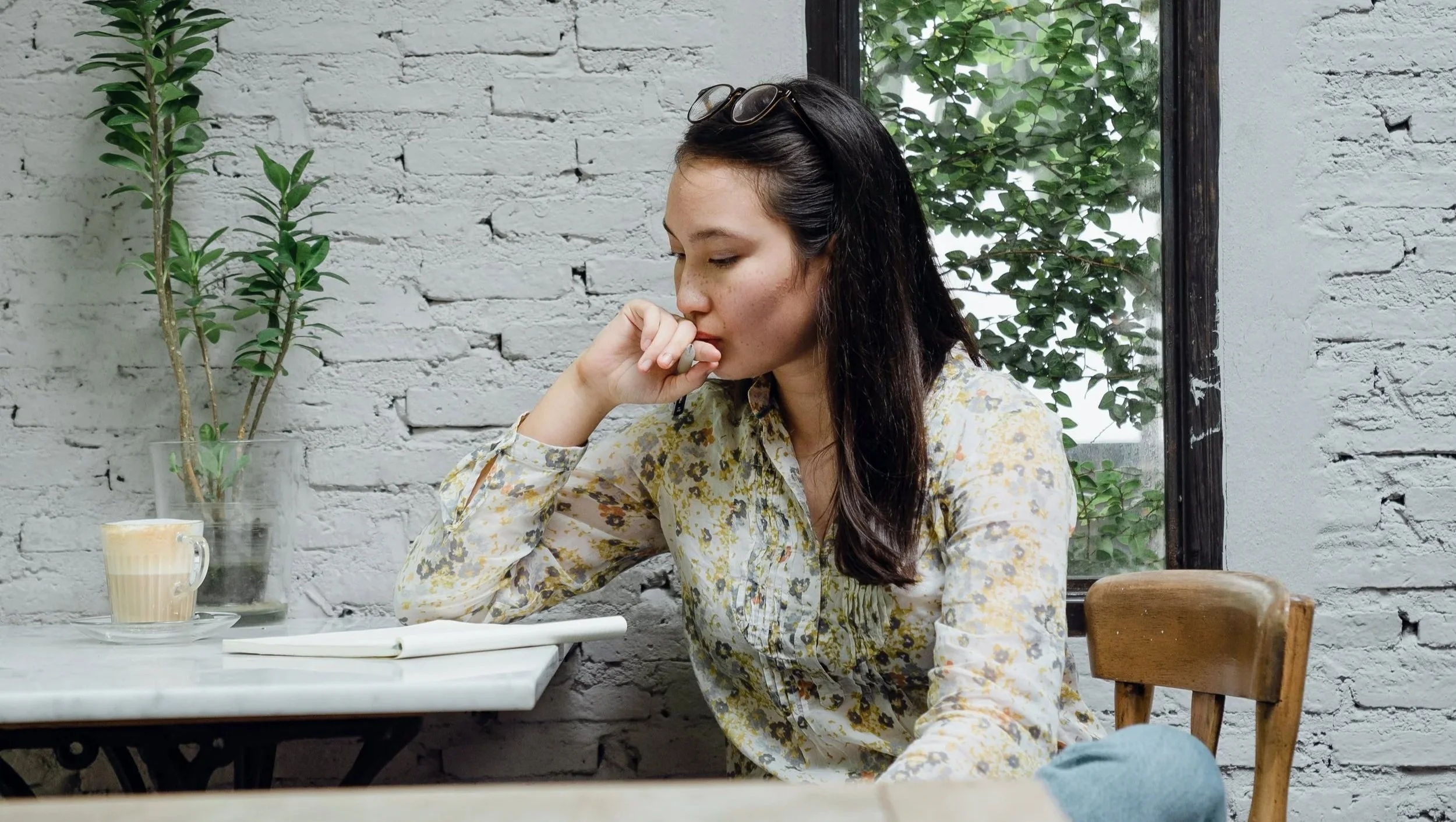 A woman sits at a table and looks pensively down at a notebook. She is considering examples for how to set boundaries to cope with burnout.