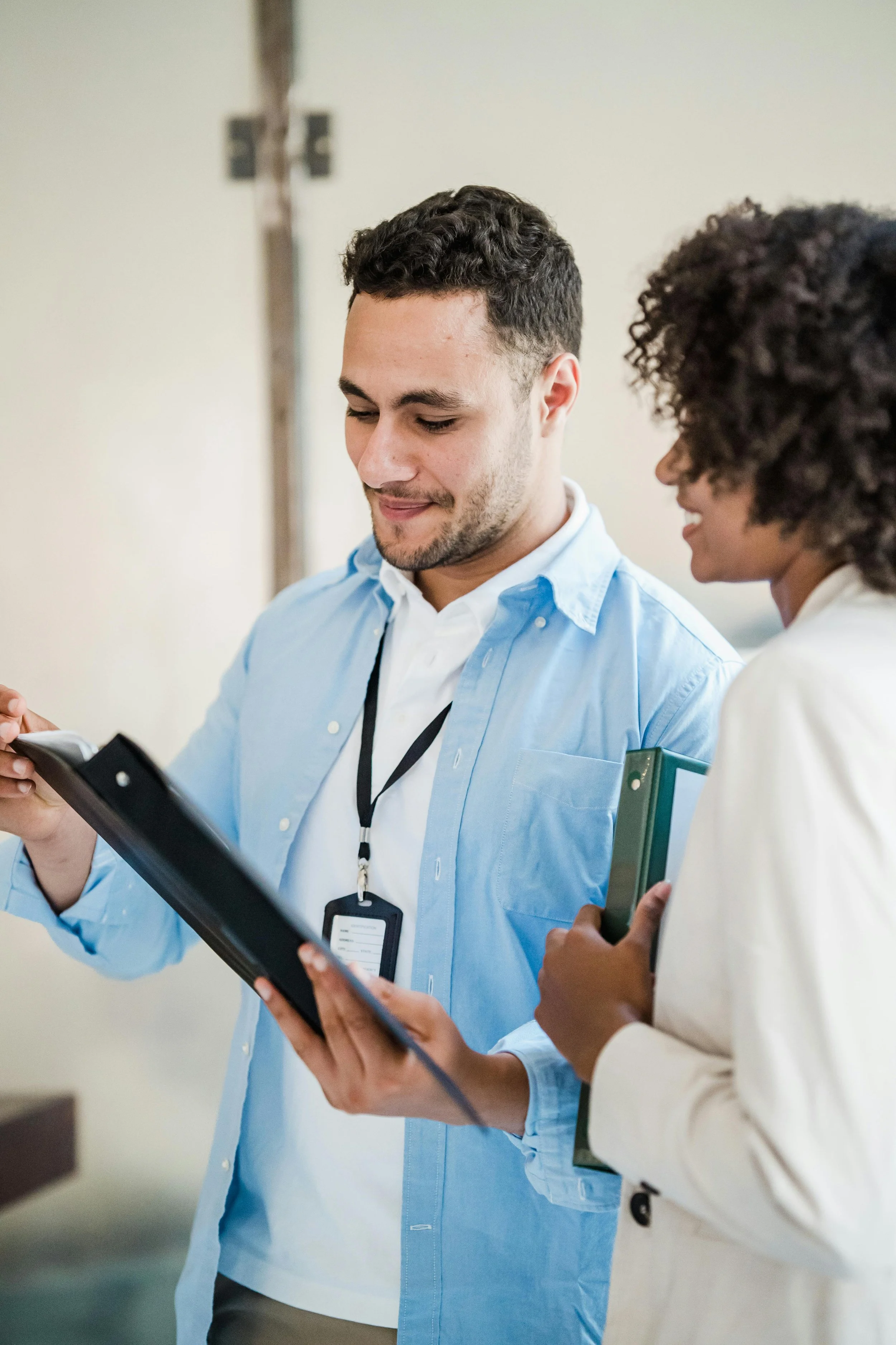 Two professionals, a man and a woman, looking at a clipboard and engaging in a discussion in a professional setting.