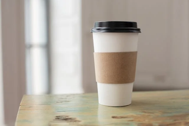 A disposable coffee cup sits on a wooden table. It represents how tired physicians are from burnout and moral injury working in our medical system.