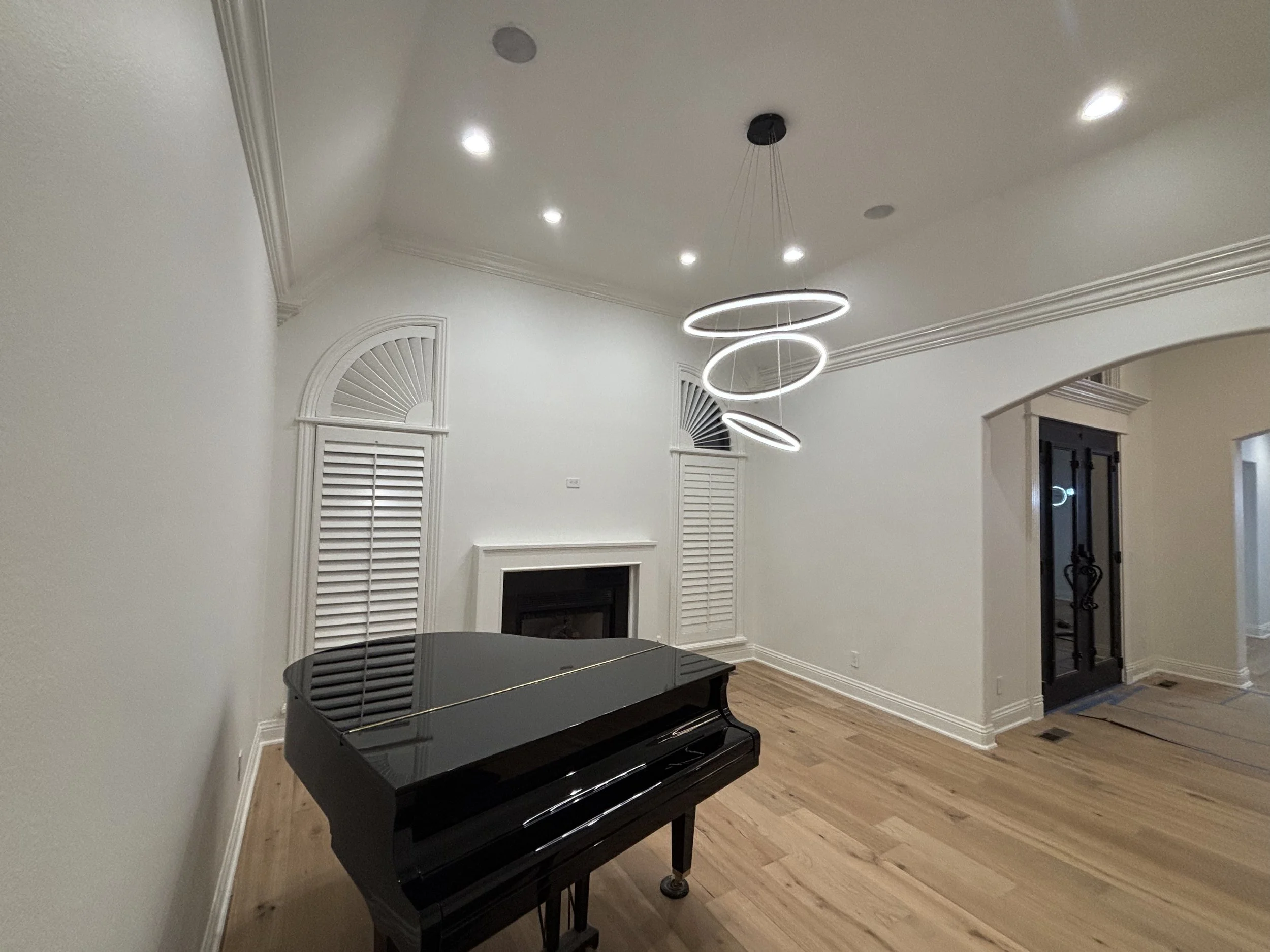 Empty living room with a black grand piano, white walls, crown molding, a fireplace, and modern ring-shaped pendant lighting.