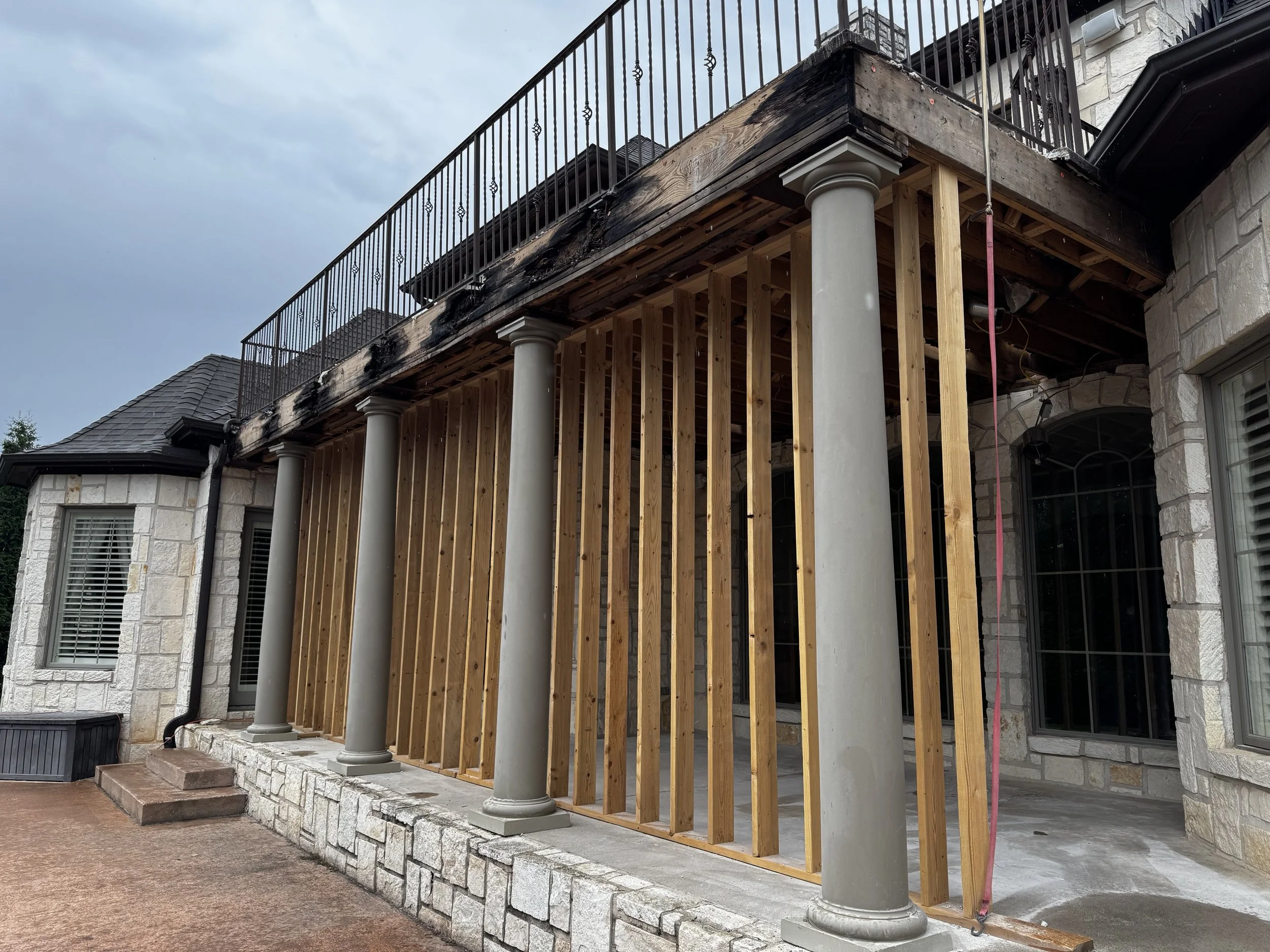 Partially constructed outdoor porch or balcony with wooden framing, gray columns, and stone exterior walls of a house.