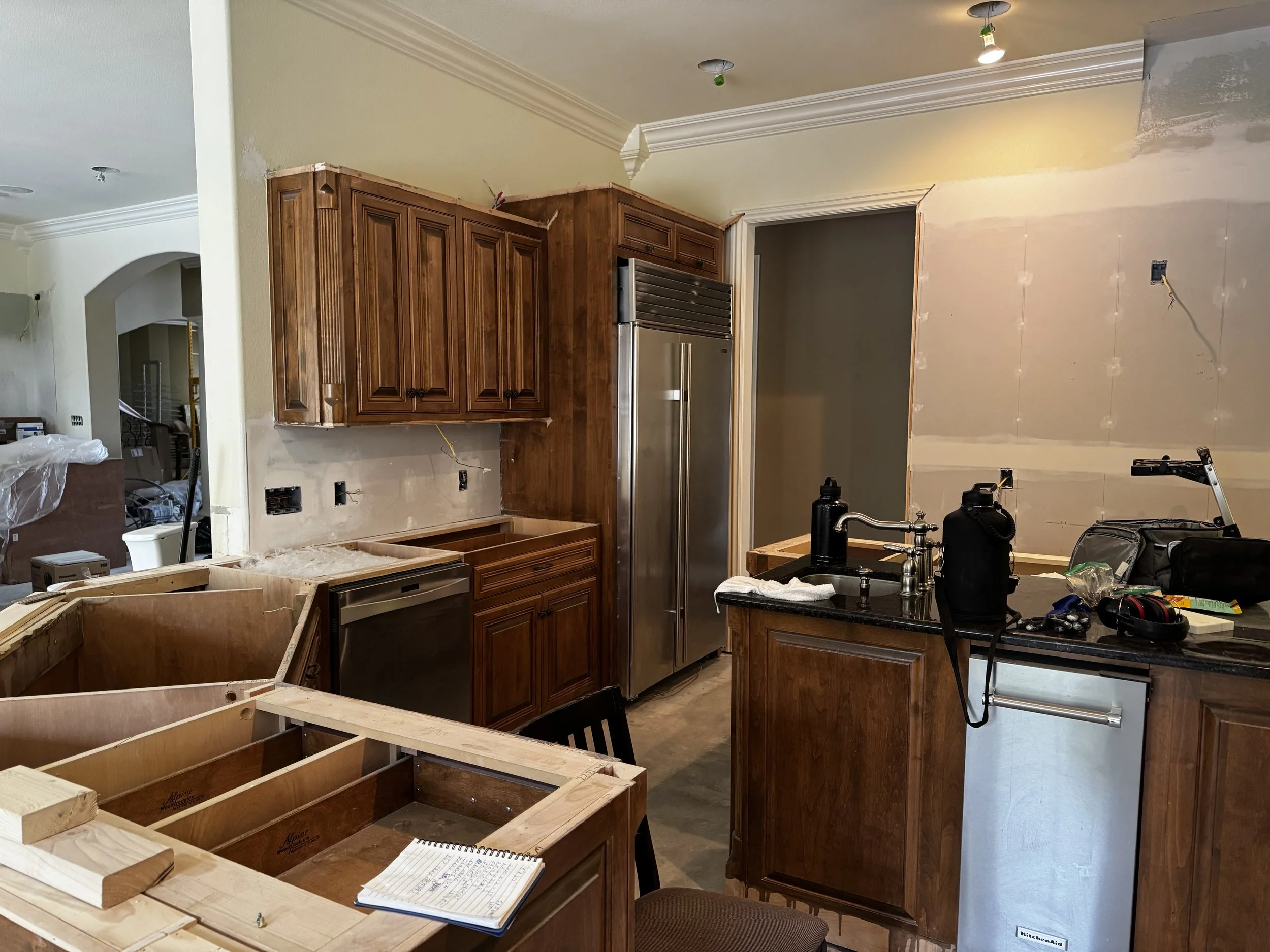 Kitchen undergoing renovation with missing cabinets, a small refrigerator, and construction tools on the countertop.