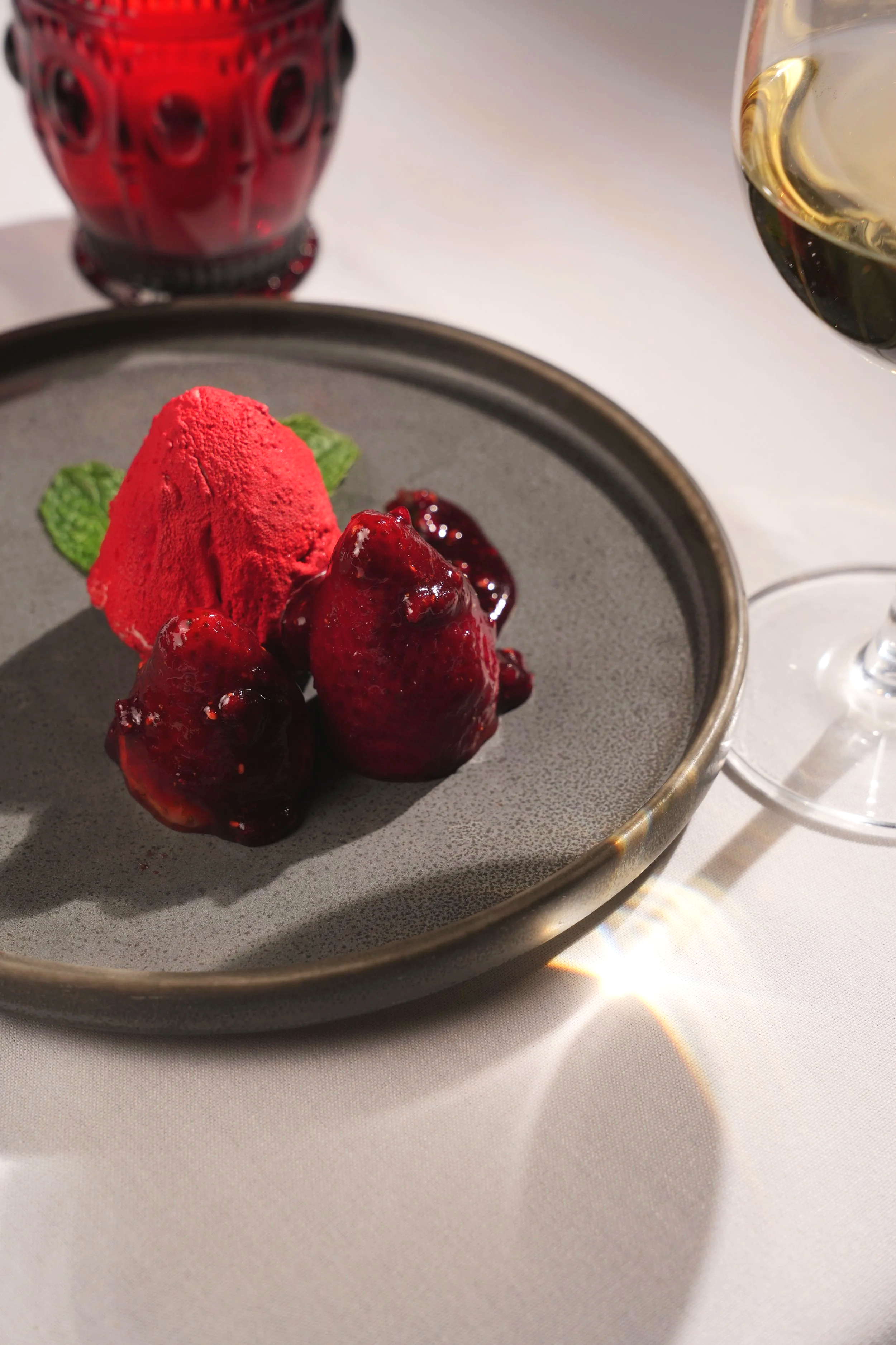 Two strawberries on a plate with strawberry glaze drizzled over the strawberries paired with a strawberry sorbet.