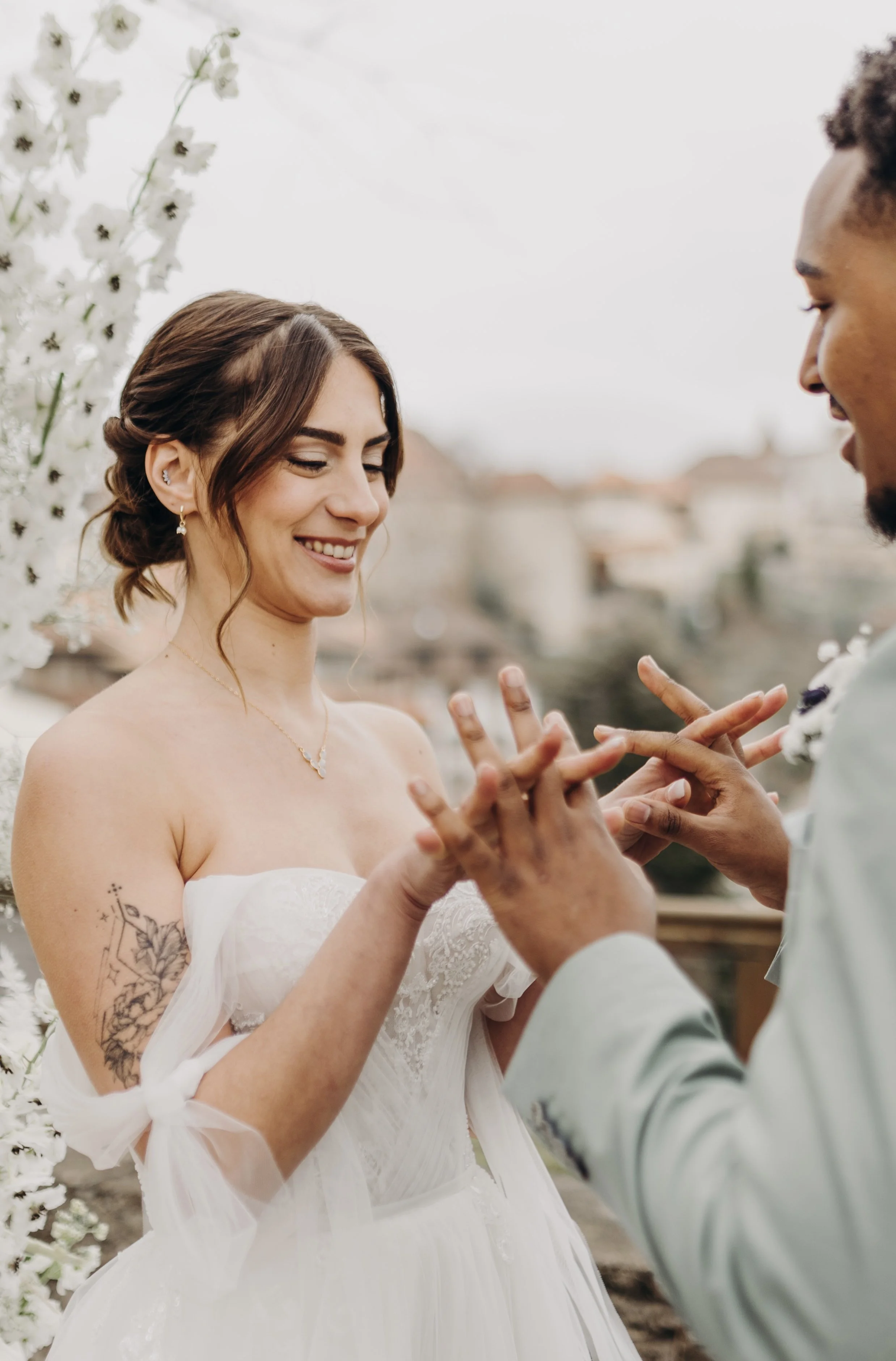 Un couple échange des vœux de mariage à l'extérieur, avec une décoration florale blanche en arrière-plan.