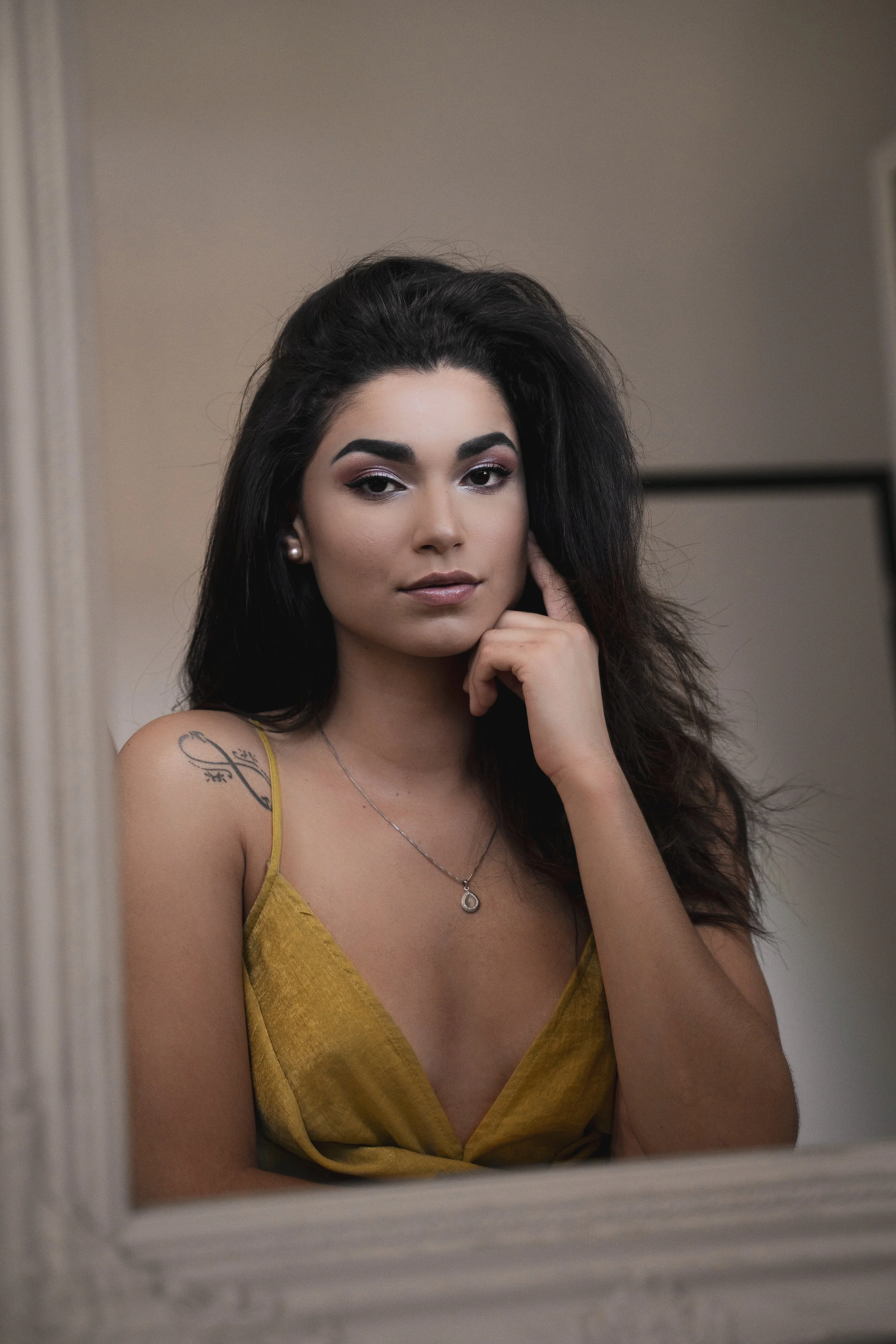 une jeune femme à la peau claire, avec des cheveux noirs, portant un haut jaune, regardant la caméra, en train de se prendre en photo dans un miroir