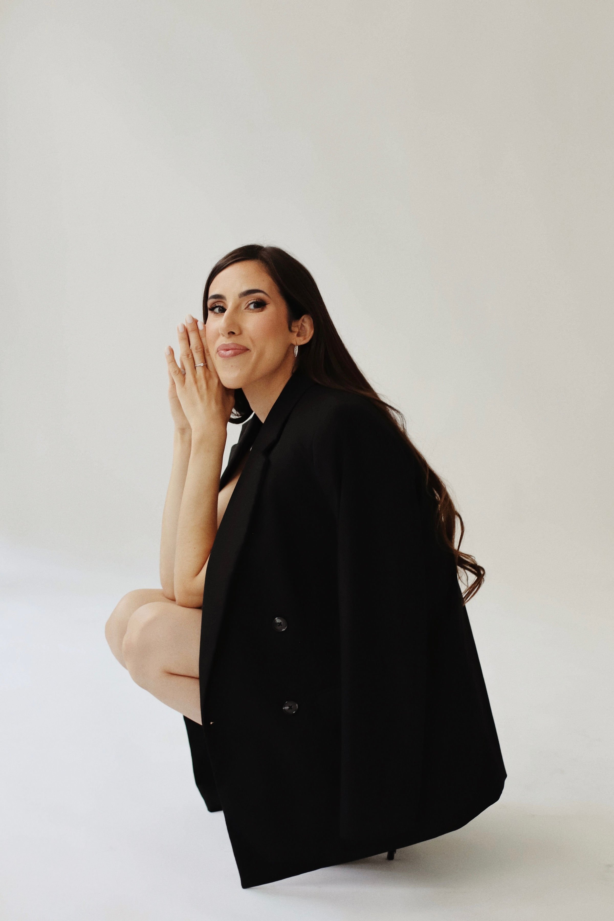 Une femme avec de longs cheveux foncés, portant une veste noire, posant sur un fond blanc.