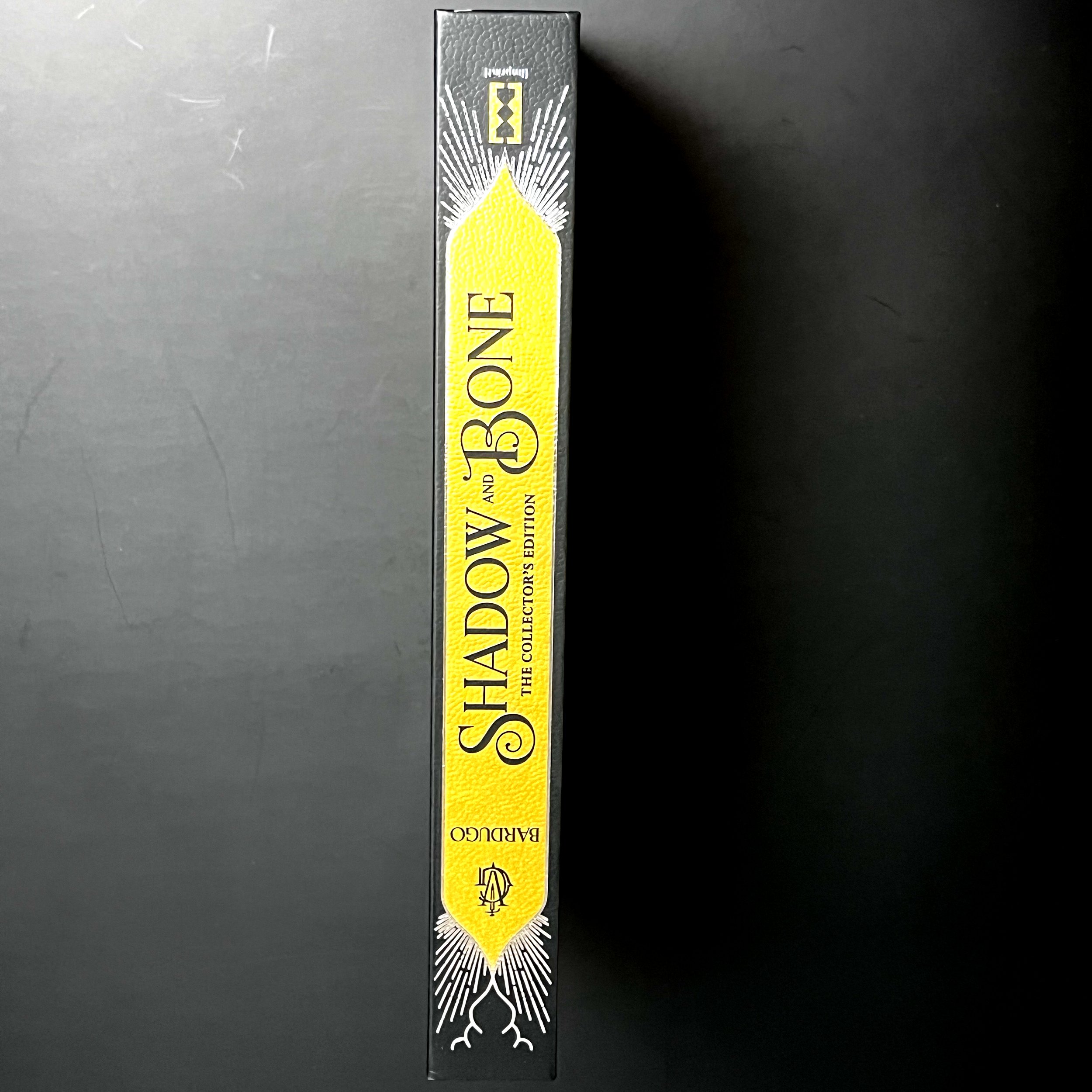 Black spine of book with a large metallic golden swatch of color with "Shadow and Bone" in black script.
